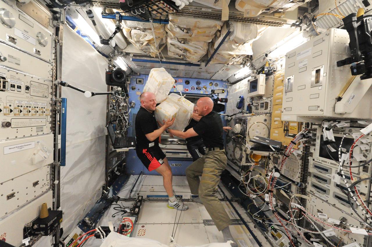 ISS040-E-076582 (25 July 2014) --- Russian cosmonaut Oleg Artemyev (left) and European Space Agency astronaut Alexander Gerst, both Expedition 40 flight engineers; along with NASA astronaut Steve Swanson (mostly obscured), commander, enjoy a light moment while moving stowage containers in the Kibo laboratory of the International Space Station.