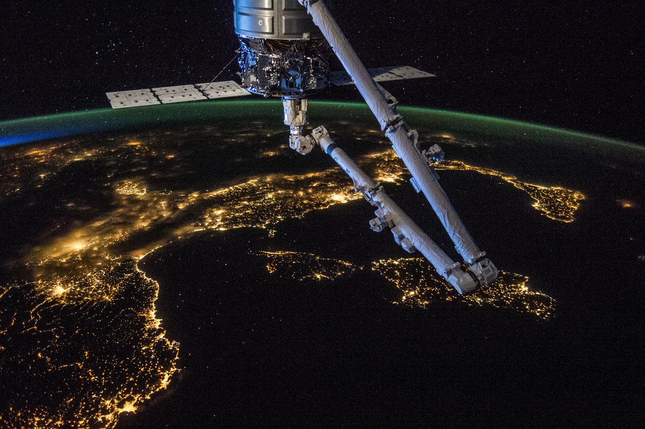 ISS040-E-081344 (26 July 2014) --- Orbital Sciences' Cygnus cargo carrier craft, in the grasp of the International Space Station's robot arm, is prominent in the foreground of this nighttime photo, taken by one of the Expedition 40 crew members aboard the orbital outpost, flying at an altitude of 225 nautical miles. Many European countries can be seen in the photo. Nearly all of Italy, from Turin (bottom left) to the island of Sicily (right center), is visible, as are the islands of Corsica and Sardinia in the Mediterranean in the center foreground. Looking across Italy over the Adriatic Sea, city lights in several other countries are visible. The 1/6 shutter speed allows for a large number of stars to be visible above the horizon.