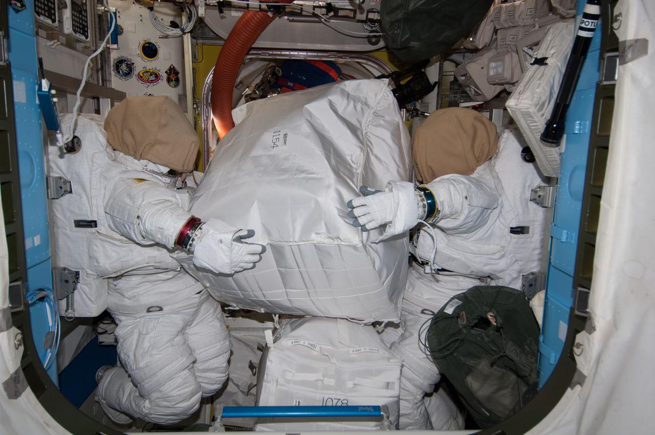 ISS040-E-086597 (1 Aug. 2014) --- Two unoccupied Extravehicular Mobility Unit (EMU) spacesuits, photographed by an Expedition 40 crew member, appear to hold stowage containers in the Quest airlock of the International Space Station.