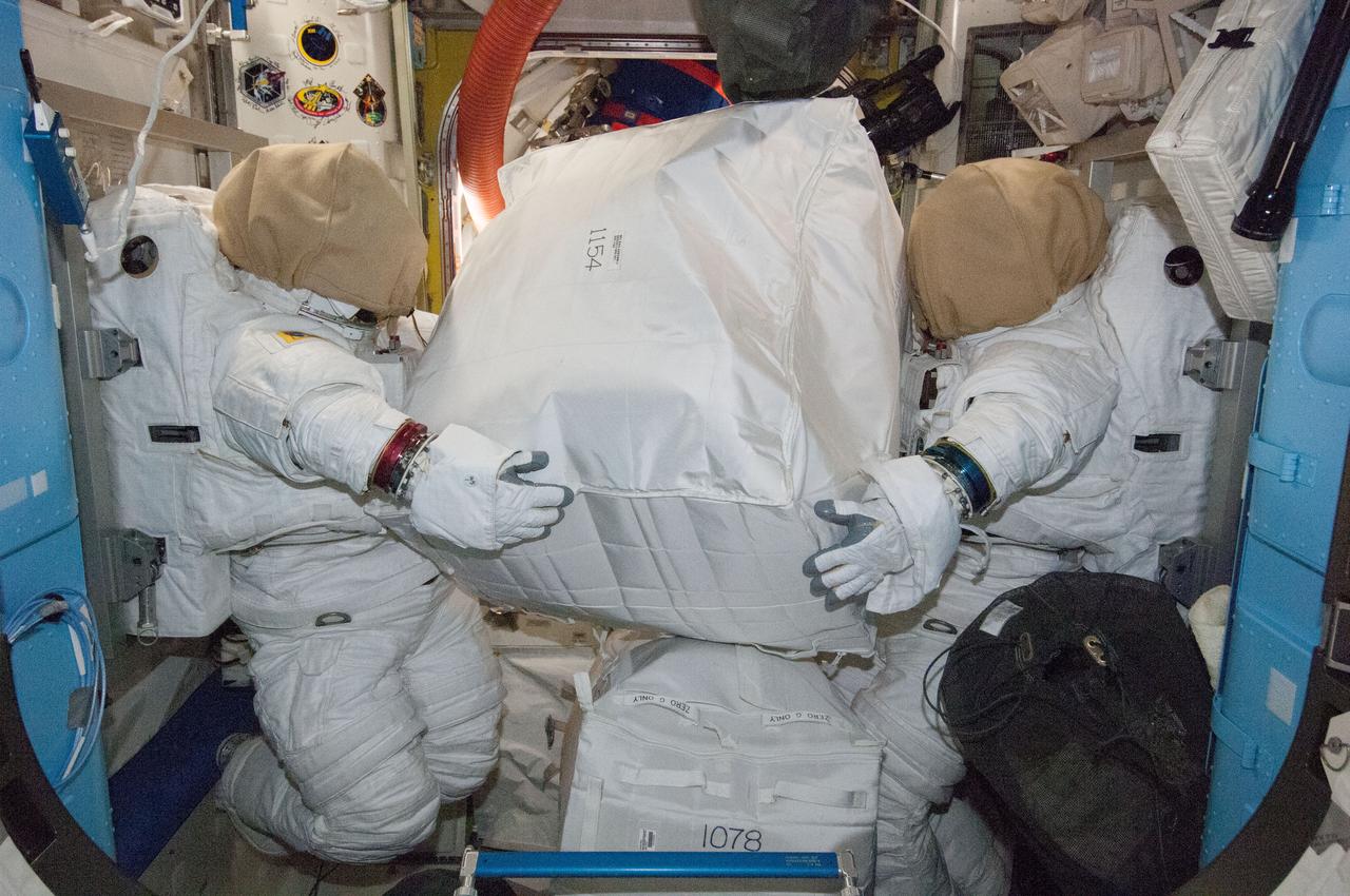 ISS040-E-086600 (1 Aug. 2014) --- Two unoccupied Extravehicular Mobility Unit (EMU) spacesuits, photographed by an Expedition 40 crew member, appear to hold stowage containers in the Quest airlock of the International Space Station.