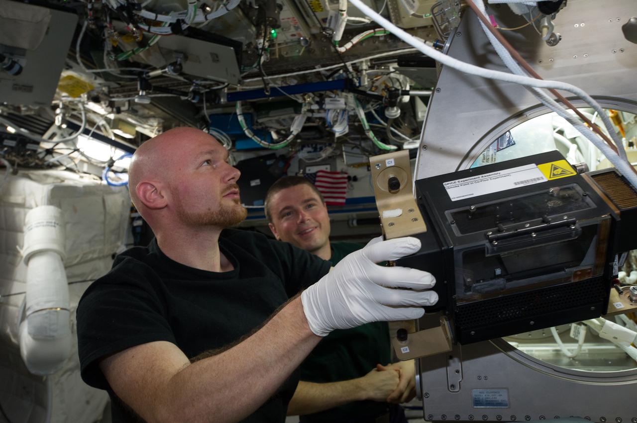 ISS040-E-088801 (5 Aug. 2014) --- European Space Agency astronaut Alexander Gerst, Expedition 40 flight engineer, removes hardware for the combustion experiment known as the Burning and Suppression of Solids (BASS-II) from the Microgravity Science Glovebox (MSG) in the Destiny laboratory of the International Space Station. The experiment seeks to provide insight on how flames burn in space compared to Earth which may provide fire safety benefits aboard future spacecraft. NASA astronaut Reid Wiseman, flight engineer, looks on.