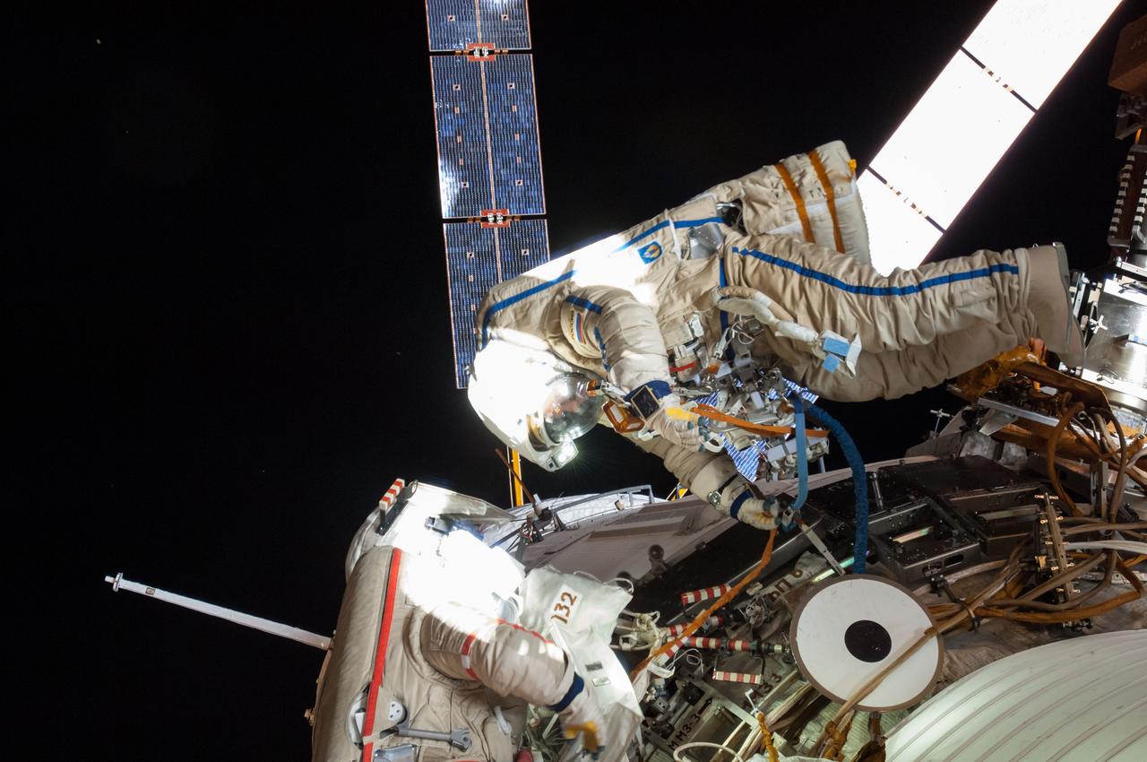 ISS040-E-099297 (18 Aug. 2014) --- Russian cosmonauts Alexander Skvortsov (left, red stripes) and Oleg Artemyev, both Expedition 40 flight engineers, attired in Russian Orlan spacesuits, participate in a session of extravehicular activity (EVA) in support of science and maintenance on the International Space Station. During the five-hour, 11-minute spacewalk, Artemyev and Skvortsov deployed a small science satellite, retrieved and installed experiment packages and inspected components on the exterior of the orbital laboratory. Solar array wings on the "Georges Lemaitre" Automated Transfer Vehicle-5 (ATV-5) docked to the Zvezda Service Module are visible in the background.