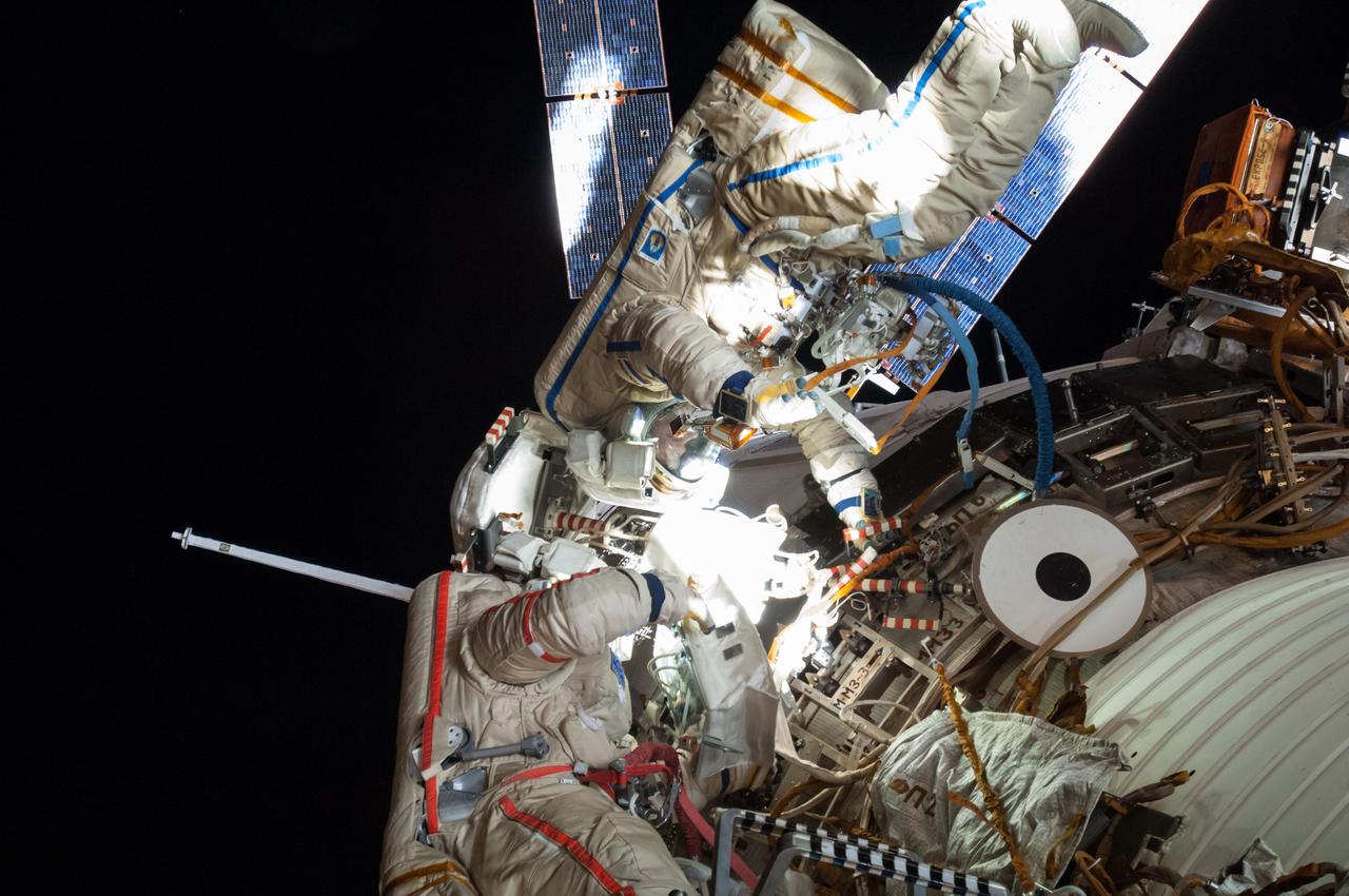 ISS040-E-099298 (18 Aug. 2014) --- Russian cosmonauts Alexander Skvortsov (left, red stripes) and Oleg Artemyev, both Expedition 40 flight engineers, attired in Russian Orlan spacesuits, participate in a session of extravehicular activity (EVA) in support of science and maintenance on the International Space Station. During the five-hour, 11-minute spacewalk, Artemyev and Skvortsov deployed a small science satellite, retrieved and installed experiment packages and inspected components on the exterior of the orbital laboratory. Solar array wings on the "Georges Lemaitre" Automated Transfer Vehicle-5 (ATV-5) docked to the Zvezda Service Module are visible in the background.