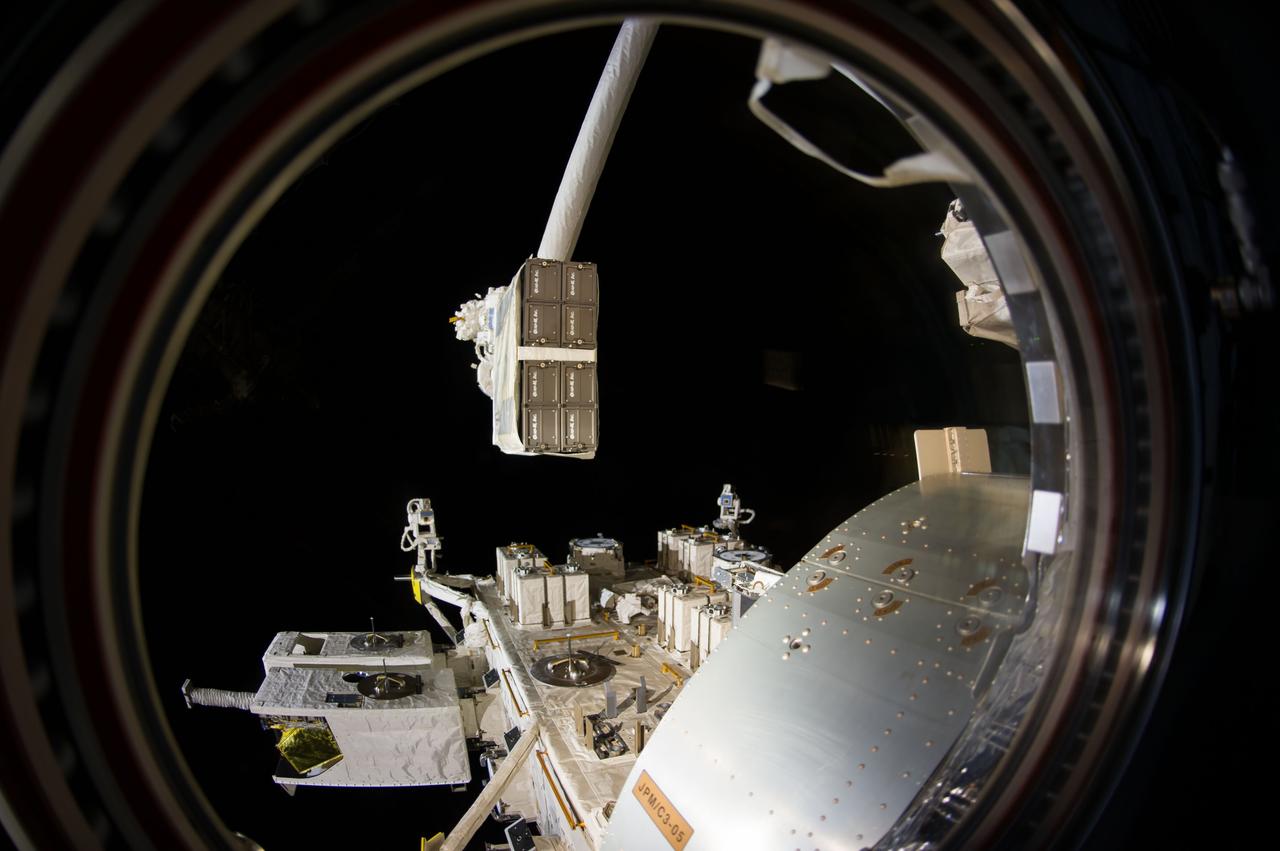 ISS040-E-100890 (19 Aug. 2014) --- Through a window in the International Space Station?s Kibo laboratory, an Expedition 40 crew member photographed the CubeSat deployer mechanism in the grasp of the Japanese robotic arm prior to a series of NanoRacks CubeSat miniature satellite deployments.