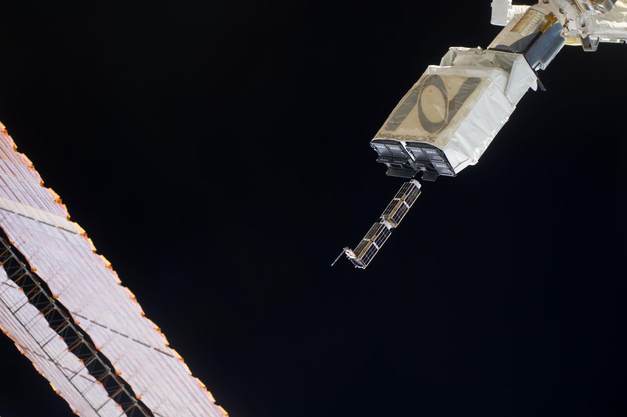 ISS040-E-102420 (20 Aug. 2014) --- In the grasp of the Japanese robotic arm, the CubeSat deployer releases a pair of NanoRacks CubeSat miniature satellites. The Planet Labs Dove satellites that were carried to the International Space Station aboard the Orbital Sciences Cygnus commercial cargo craft are being deployed between Aug. 19 and Aug. 25. A section of the station solar array wings is at left.