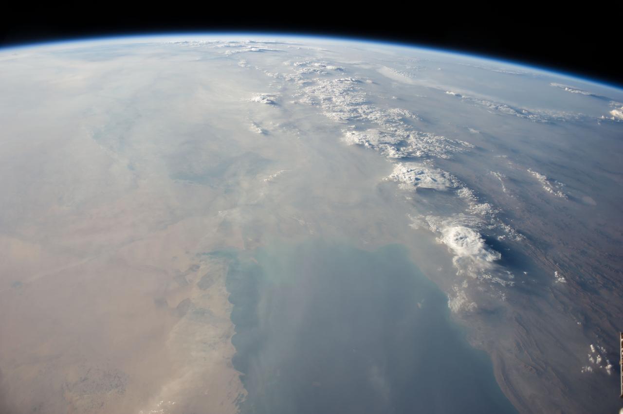 ISS040-E-113700 (31 Aug. 2014) --- This panorama view, photographed by an Expedition 40 crew member on the International Space Station, shows tan-colored dust of a major dust storm obscuring the Persian Gulf and the its northern shoreline. Strong north winds often blow in summer, churning up dust from the entire length of the desert surfaces of the Tigris and Euphrates valleys (top left). Dust partly obscures the hundreds of kilometers of Iraq’s light-green agricultural lands along these rivers (left). A line of thunderstorms is being set off by the Zagros Mountains of Iran (right), with the setting sun casting long shadows from the thunderheads. Space station crews see sixteen sunrises and sunsets every day from low Earth orbit. Here the crew captured dusk in a darkening Iranian landscape (right).