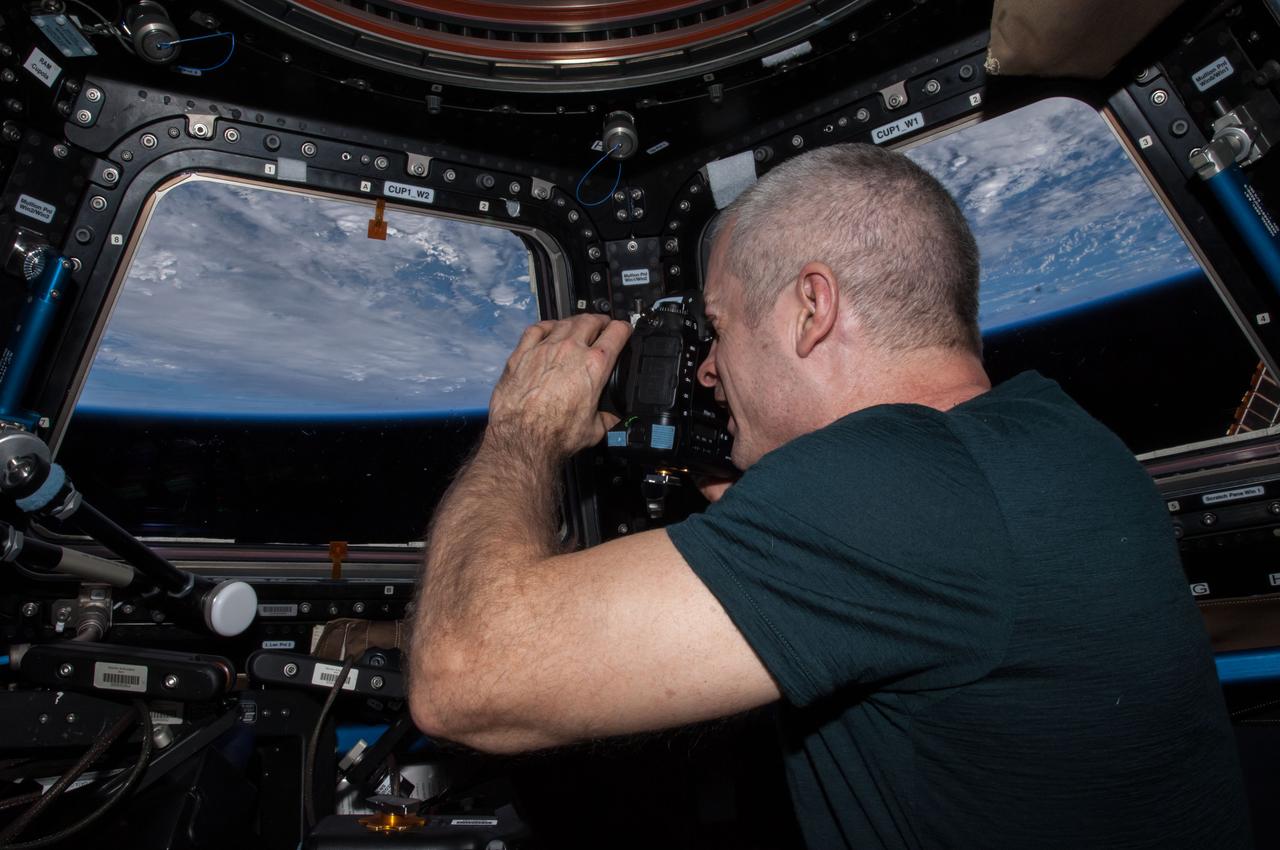 ISS040-E-123646 (7 Sept. 2014) --- NASA astronaut Steve Swanson, Expedition 40 commander, uses a still camera at the windows in the Cupola of the International Space Station. A blue and white part of Earth and the blackness of space are visible through the windows.