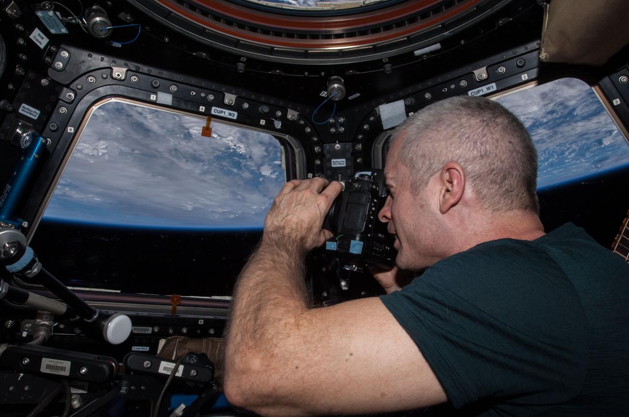 ISS040-E-123647 (7 Sept. 2014) --- NASA astronaut Steve Swanson, Expedition 40 commander, uses a still camera at the windows in the Cupola of the International Space Station. A blue and white part of Earth and the blackness of space are visible through the windows.