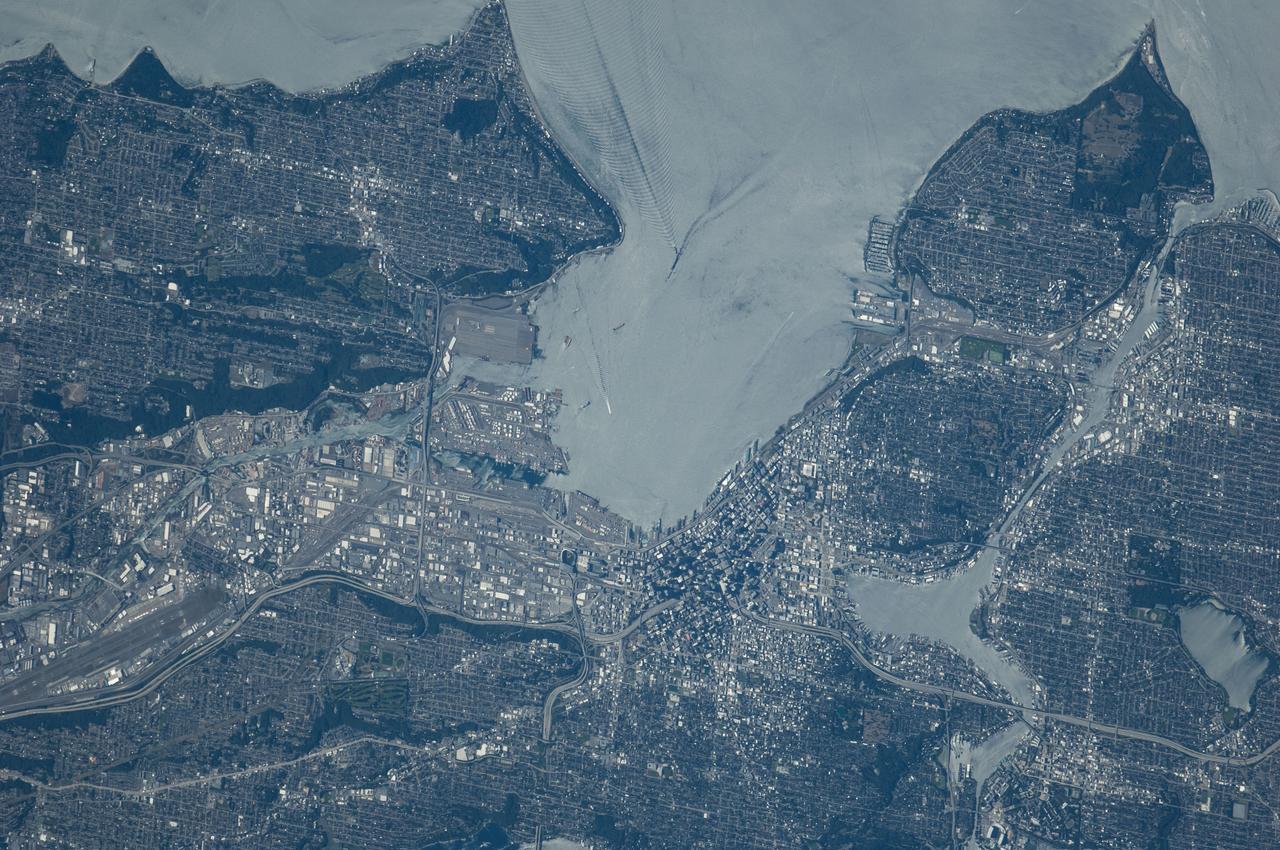 ISS040-E-124198 (6 Sept. 2014) --- Puget Sound is partly reflecting the sun in this detailed image taken by an Expedition 40 crew member on the International Space Station. Patterns of boat wakes are prominent in the sun’s partial reflection zone. The difference between the boat wakes in this view relates to the speed of the boat and the particular patterns (of several) that happen to be captured in the specific light reflection angles at the time the image was taken. The land areas show parts of Seattle. The darkest areas with rectangular grids are suburbs richly covered with trees. The broadly gray zones of the central city (bottom center) are brighter where structures are lower, as in the harbor zone (Harbor Island), and darker where the shadows of high-rise buildings downtown cast black shadows. Interstate Highway 5 bisects downtown.