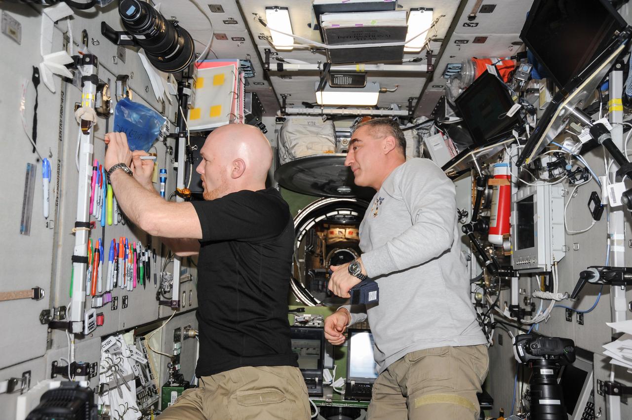 ISS040-E-130021 (9 Sept. 2014) --- European Space Agency astronaut Alexander Gerst (left), writes a note while Russian cosmonaut Alexander Skvortsov, both Expedition 40 flight engineers, looks on in the Zvezda Service Module of the International Space Station.