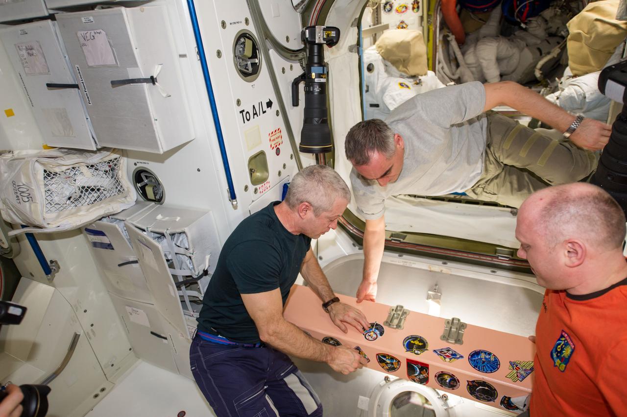 ISS040-E-139592 (9 Sept. 2014) --- In the Unity node, NASA astronaut Steve Swanson (left), Expedition 40 commander, adds the Expedition 40 patch to the growing collection of insignias representing crews who have worked on the International Space Station. Russian cosmonauts Alexander Skvortsov (center) and Oleg Artemyev, both flight engineers, look on.