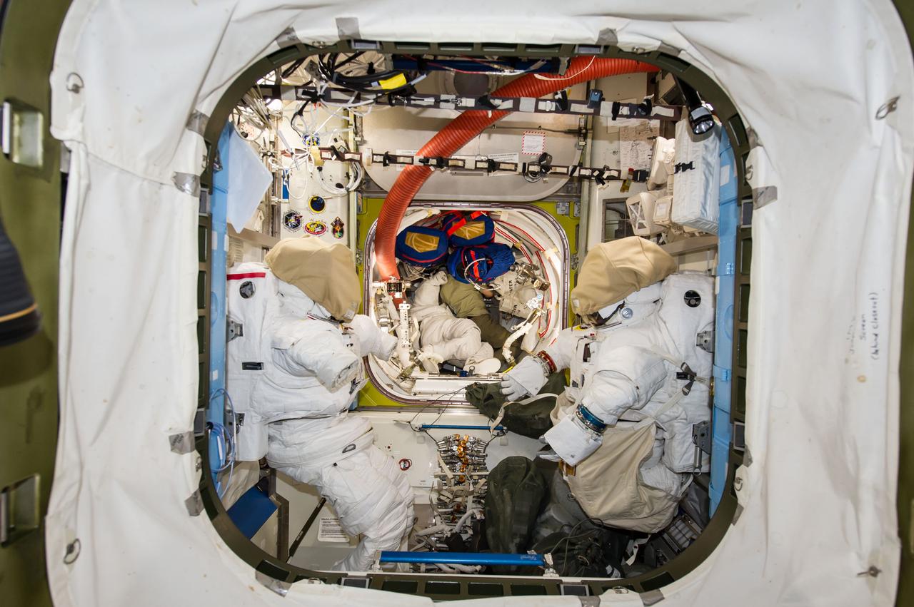 ISS041-E-016635 (16 Sept. 2014) --- NASA astronaut Reid Wiseman (center background), Expedition 41 flight engineer, works among stowed equipment in the Quest airlock of the International Space Station. Two Extravehicular Mobility Unit (EMU) spacesuits are visible in the foreground.