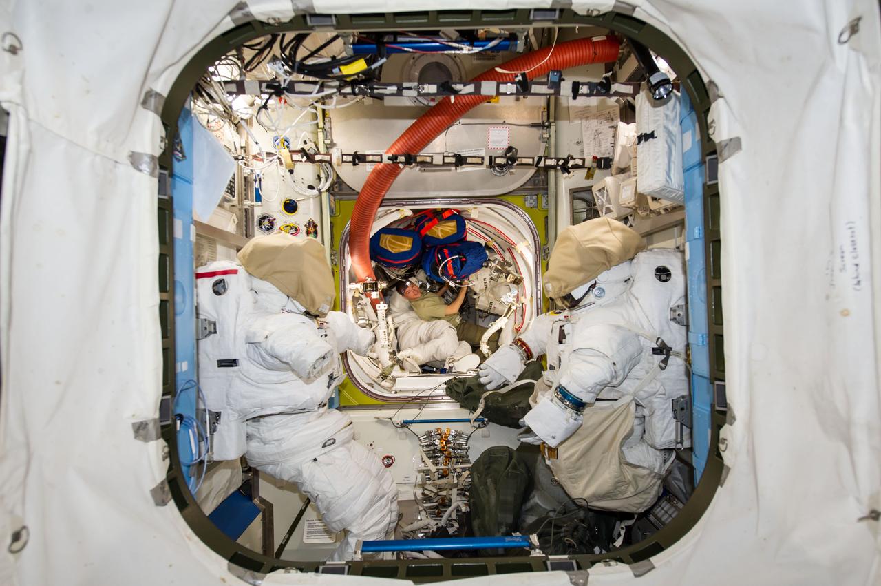 ISS041-E-016637 (16 Sept. 2014) --- NASA astronaut Reid Wiseman (center background), Expedition 41 flight engineer, works among stowed equipment in the Quest airlock of the International Space Station. Two Extravehicular Mobility Unit (EMU) spacesuits are visible in the foreground.