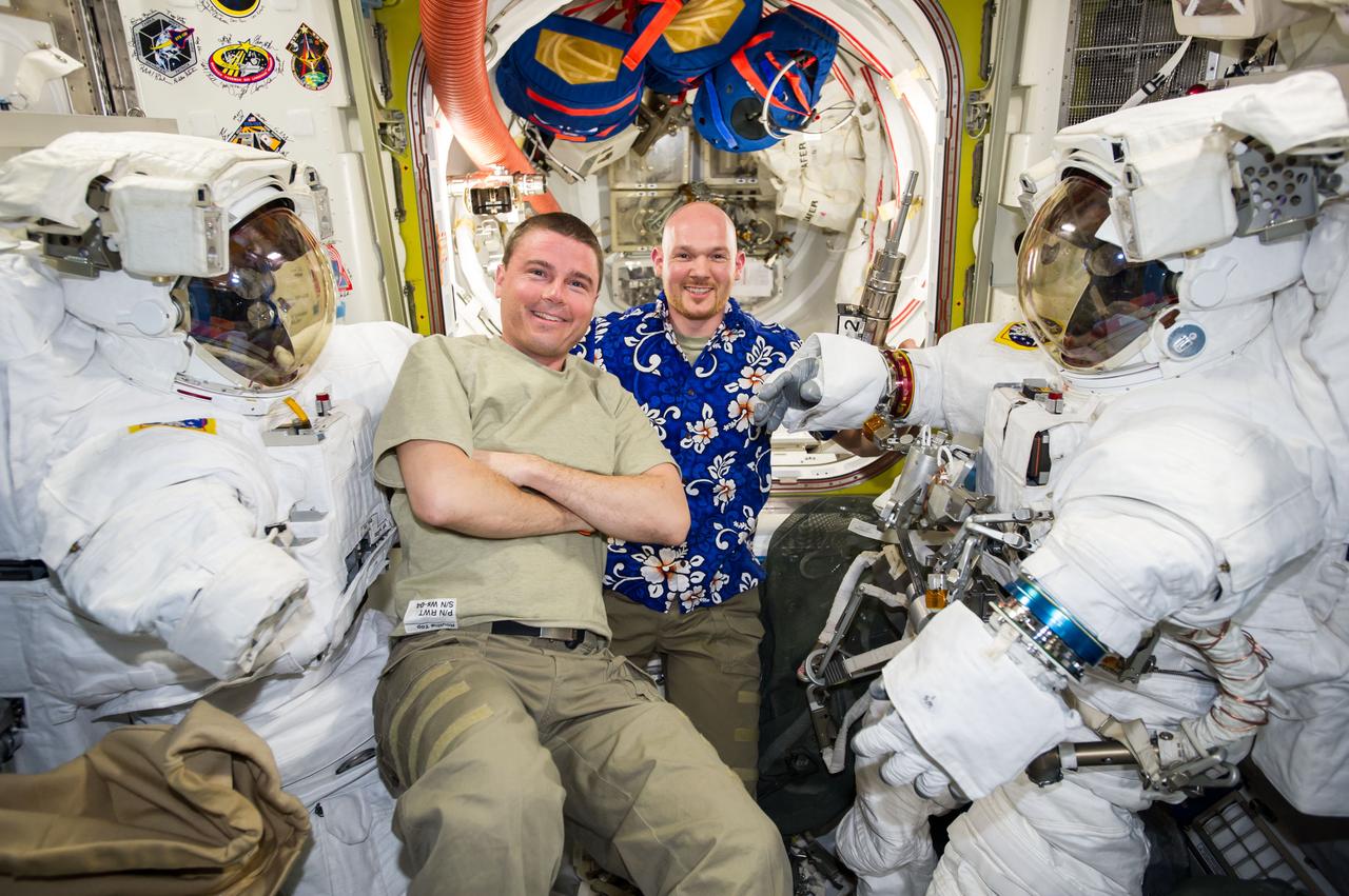 ISS041-E-017047 (19 Sept. 2014) --- NASA astronaut Reid Wiseman (left) and European Space Agency astronaut Alexander Gerst, both Expedition 41 flight engineers, take a moment to pose for a photo with two Extravehicular Mobility Unit (EMU) spacesuits in the Quest airlock of the International Space Station while preparing for two spacewalks scheduled in October 2014.