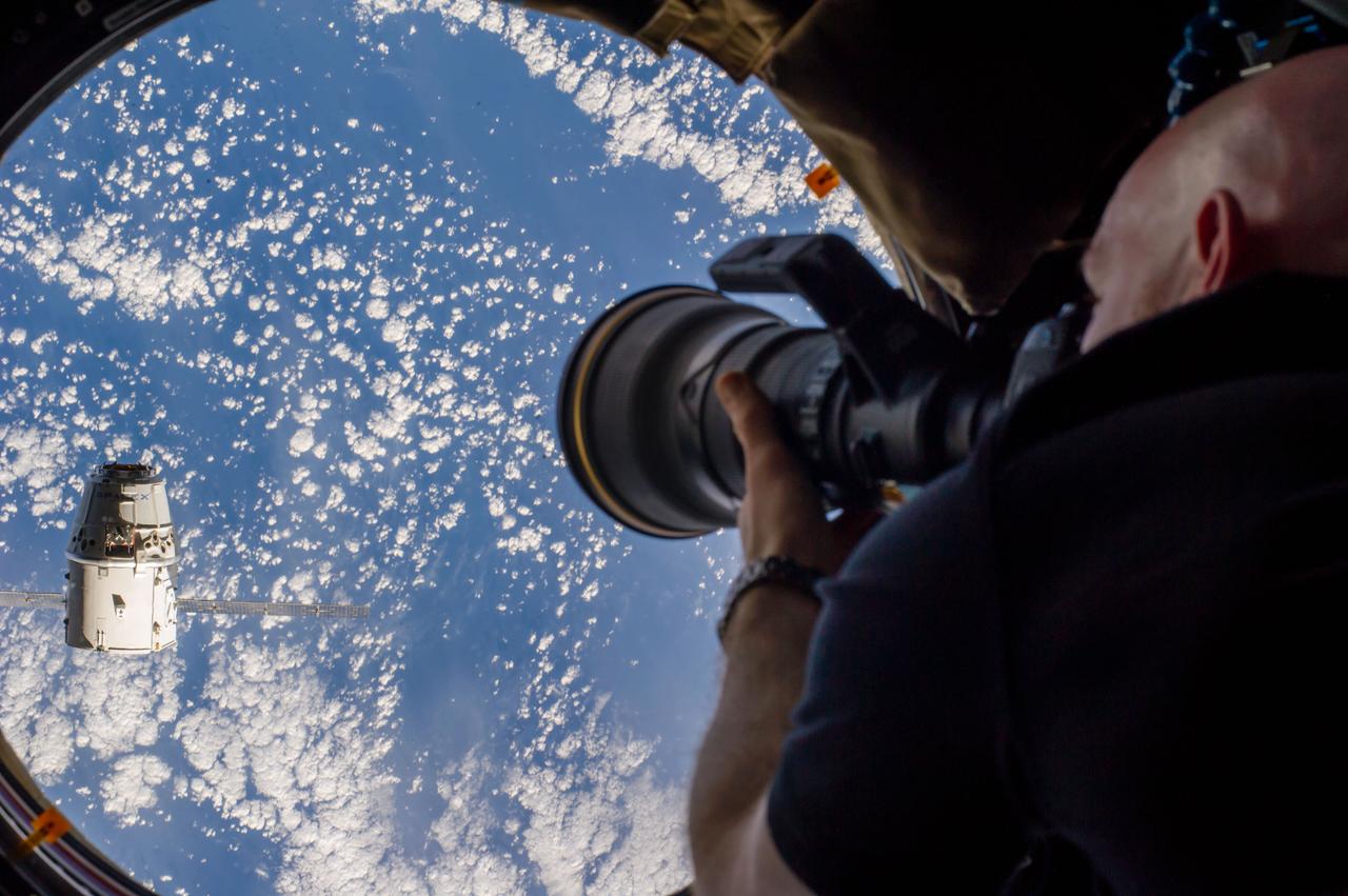 ISS041-E-020816 (23 Sept. 2014) --- European Space Agency astronaut Alexander Gerst, Expedition 41 flight engineer, uses a still camera at a window in the Cupola of the International Space Station as the SpaceX Dragon commercial cargo craft approaches the International Space Station on Sept. 23, 2014.
