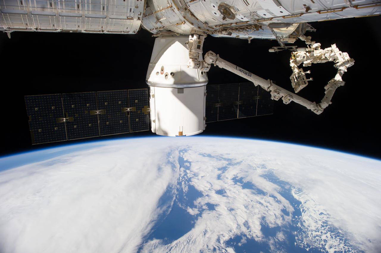 ISS041-E-047455 (29 Sept. 2014) --- An Expedition 41 crew member aboard the International Space Station photographed this view of the SpaceX Dragon cargo ship docked to the nadir port of the Harmony node as the station's Canadarm2 and the Special Purpose Dexterous Manipulator move external cargo from Dragon. A blue and white part of Earth and the blackness of space provide the backdrop for the scene.