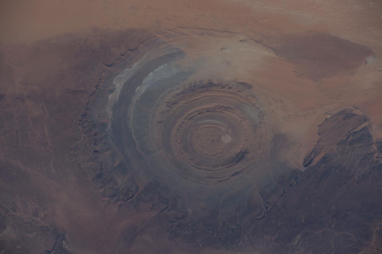 ISS042E007131 (11/22/2014) — Astronauts aboard the International Space Station captured this image of a huge crater in Africa on Nov. 22, 2014. This is the Richat Structure in northwestern Mauritania, otherwise known as the “Eye of the Sahara.” Scientists are still deciding whether this was formed by a subterranean volcano or impact from a large meteor. Deep in the Sahara Desert it is nearly a perfect circle, it is 1.2 miles (1.9 kilometers) wide, and sports a rim 330 feet (100 meters) tall. The crater sits in a vast plain of rocks so ancient they were deposited hundreds of millions of years before the first dinosaurs walked the Earth.