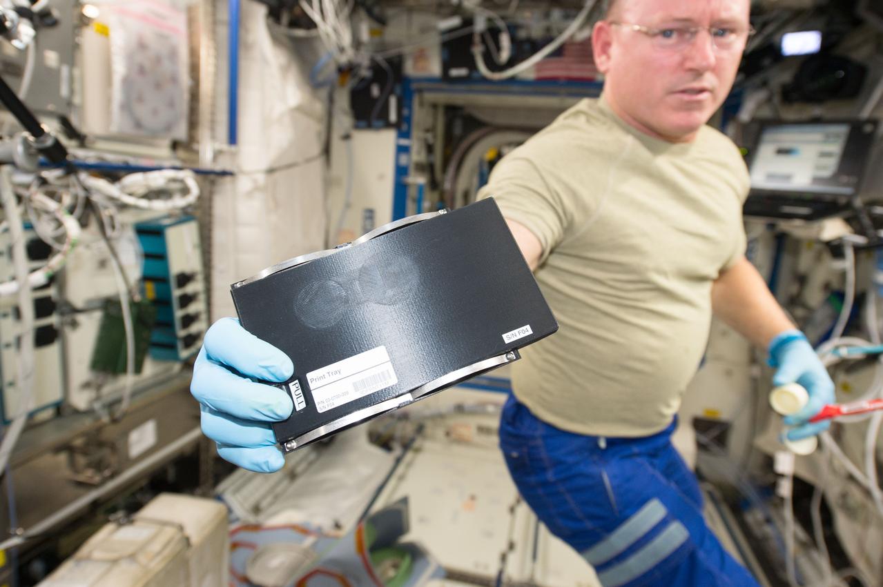 iss042e031282 (12/09/2014) ---US Astronaut Barry (Butch) Wilmore holding a 3D coupon works with the new 3D printer aboard the International Space Station. The 3D Printing experiment in zero gravity  demonstrates that a 3D printer works normally in space. In general, a 3D printer extrudes streams of heated plastic, metal or other material, building layer on top of layer to create 3 dimensional objects. Testing a 3D printer using relatively low-temperature plastic feedstock on the International Space Station is the first step towards establishing an on-demand machine shop in space, a critical enabling component for deep-space crewed missions and in-space manufacturing.