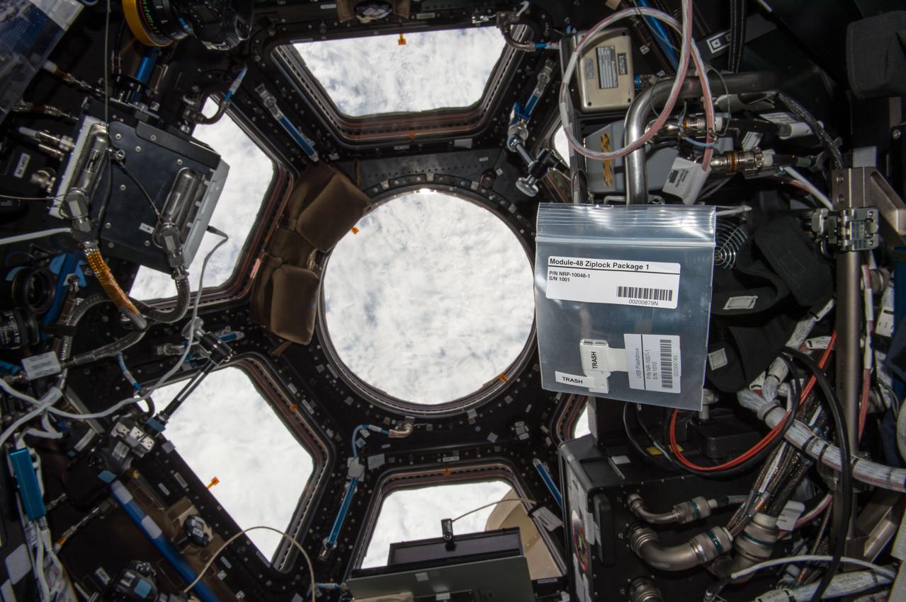 iss042e182203 (1/27/2017) --- A view of items from the NanoRacks-Lagrange investigation floating in front of the  windows in the Cupola module aboard the International Space Station (ISS). NanoRacks-Lagrange seeks to increase interest in space. For this investigation, student photos and printed logos sheets are launched to the International Space Station (ISS) with a message card. Additionally, plant seeds are flown to the ISS. The students plant the seeds once they return to Earth and compare them to plants grown from regular seeds. Students are able to touch and feel close to space through this experiment.