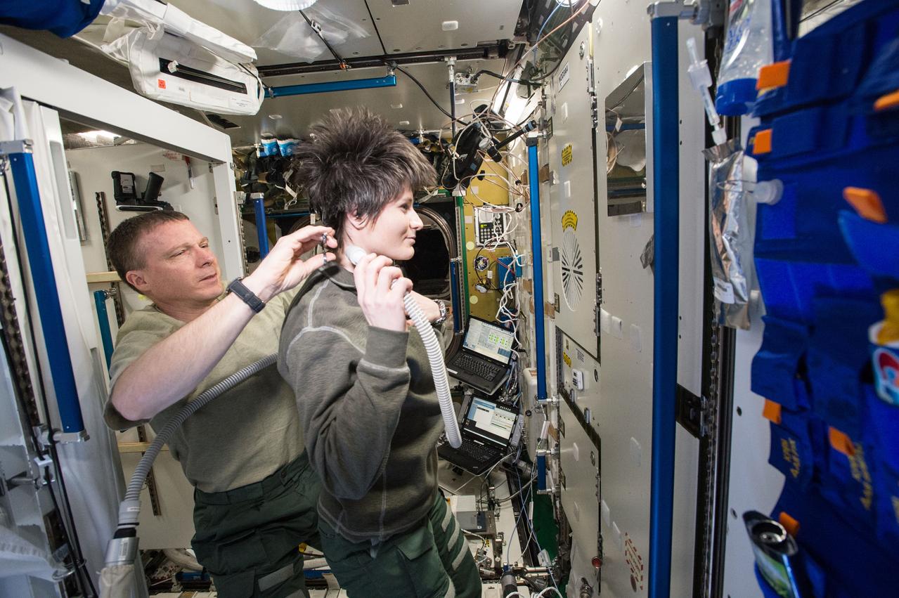 Caption: ISS043E044174 (03/22/2015) --- Its haircut time onboard the International Space Station as Expedition 43 Commander and NASA astronaut Terry Virts handles the scissors while ESA (European Space Agency) astronaut Samantha Cristoforetti holds the vacuum to immediately pull the fine hair strands into the safe container so they don't float away into the station. Hair trims are a regular occurrence during an astronaut's six month tour.
