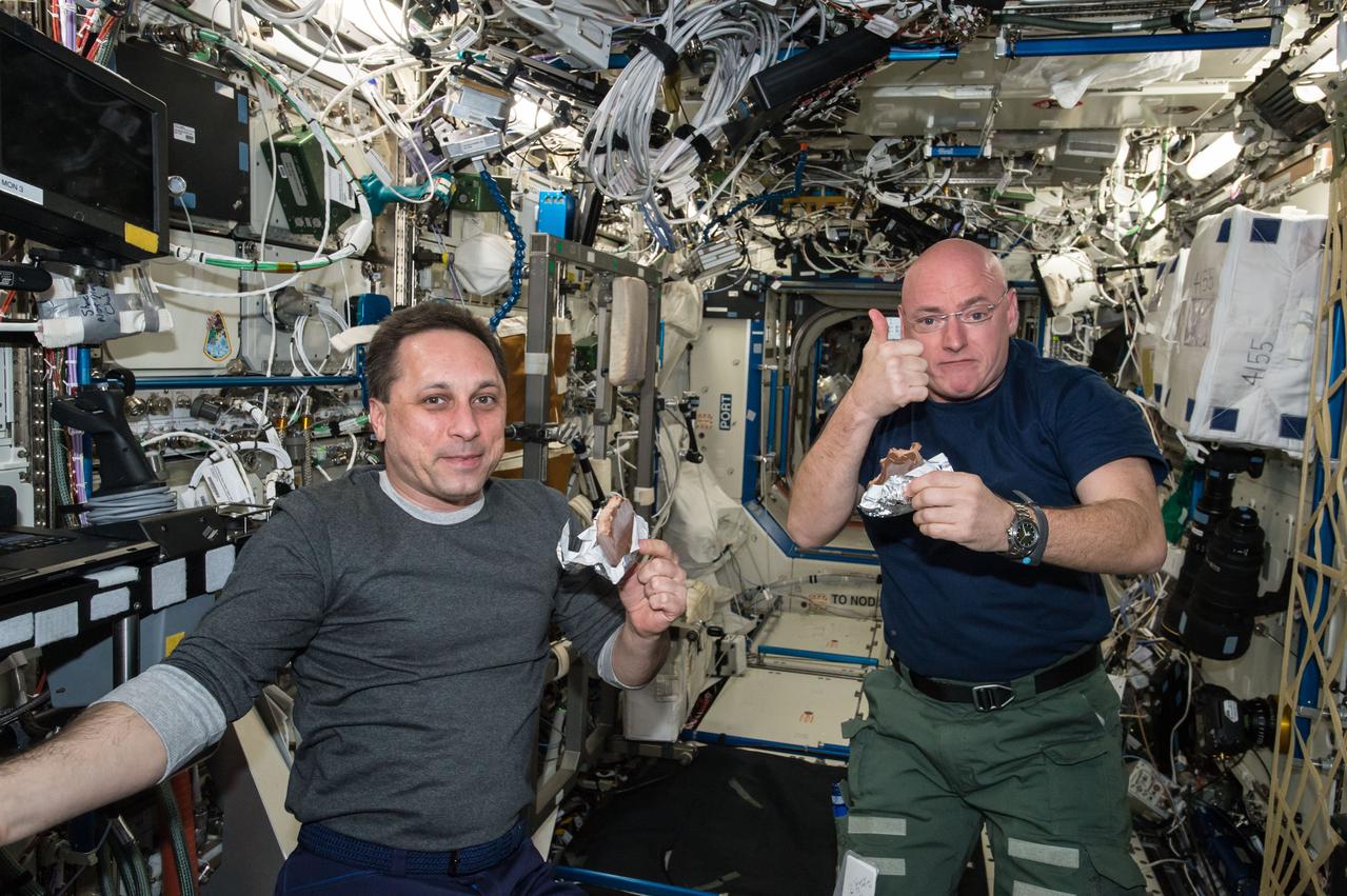 ISS043E125774 (04/20/2015) --- NASA astronaut Scott Kelly gives the "high sign" on the quality of his snack while taking a break from his work schedule aboard the International Space Station on Apr. 20, 2015. Russian cosmonaut Anton Shkaplerov (ROSCOSMOS) seems to agree on the tasty factor of the specially prepared space food.
