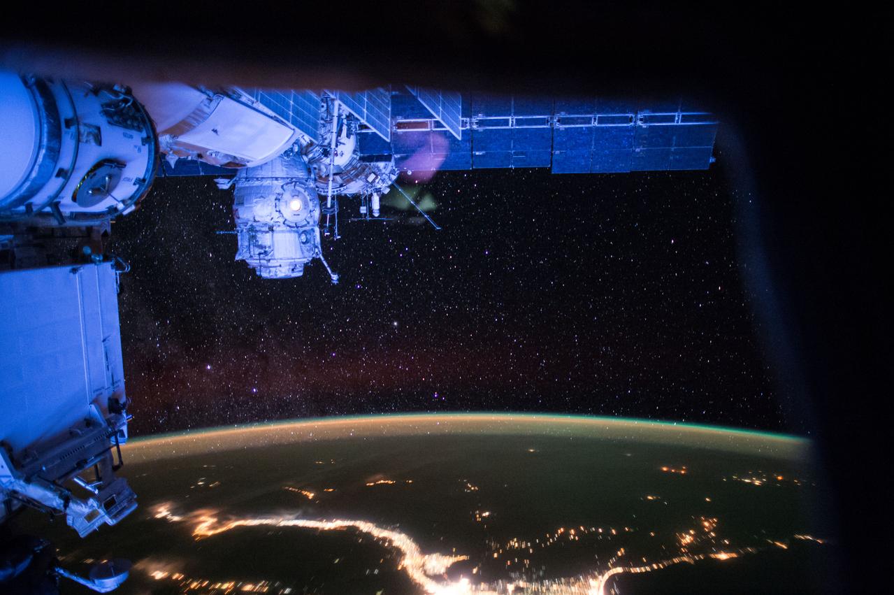 ISS043E218074 (05/18/2015) --- This night view from the International Space Station on May 18, 2015 gives a view of brilliant city lights on the Earth’s surface shining beneath thousands of stars above. The thin line of Earth’s atmosphere can be seen with the green glow of aurora along the outer edge.