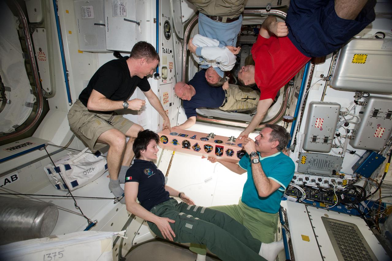 ISS043E270899 (05/30/2015) --- The Expedition 43 crew gathers aboard the International Space Station to affix their mission patch to the vehicle. In view is Commander Terry Virts (center left), Scott Kelly (top left), Gennady Padalka (top center), Anton Shkaplerov (top right), Mikhail Kornienko (bottem right),  Samantha Cristoforetti (bottom center)