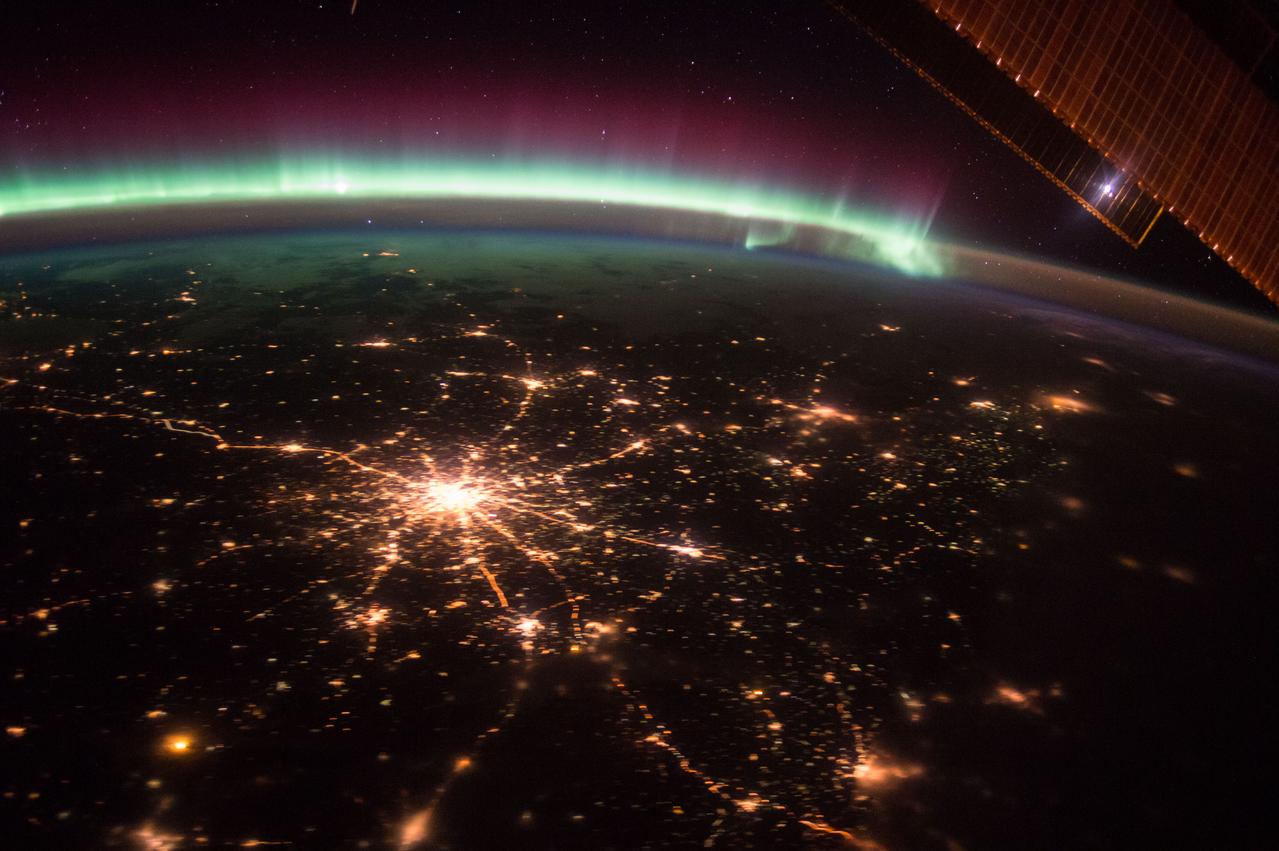 ISS045E048653 (10/06/2015) --- The International Space Station crew witness nightly scenes of our Earths beauty after performing their duties. Here on Oct. 6, 2015, framed by the edge of a huge Station solar panel, the city of Moscow Russia sparkles in the night with spoke streets streaming out across the land while an aurora of blue white and purple contrast the star filled sky.