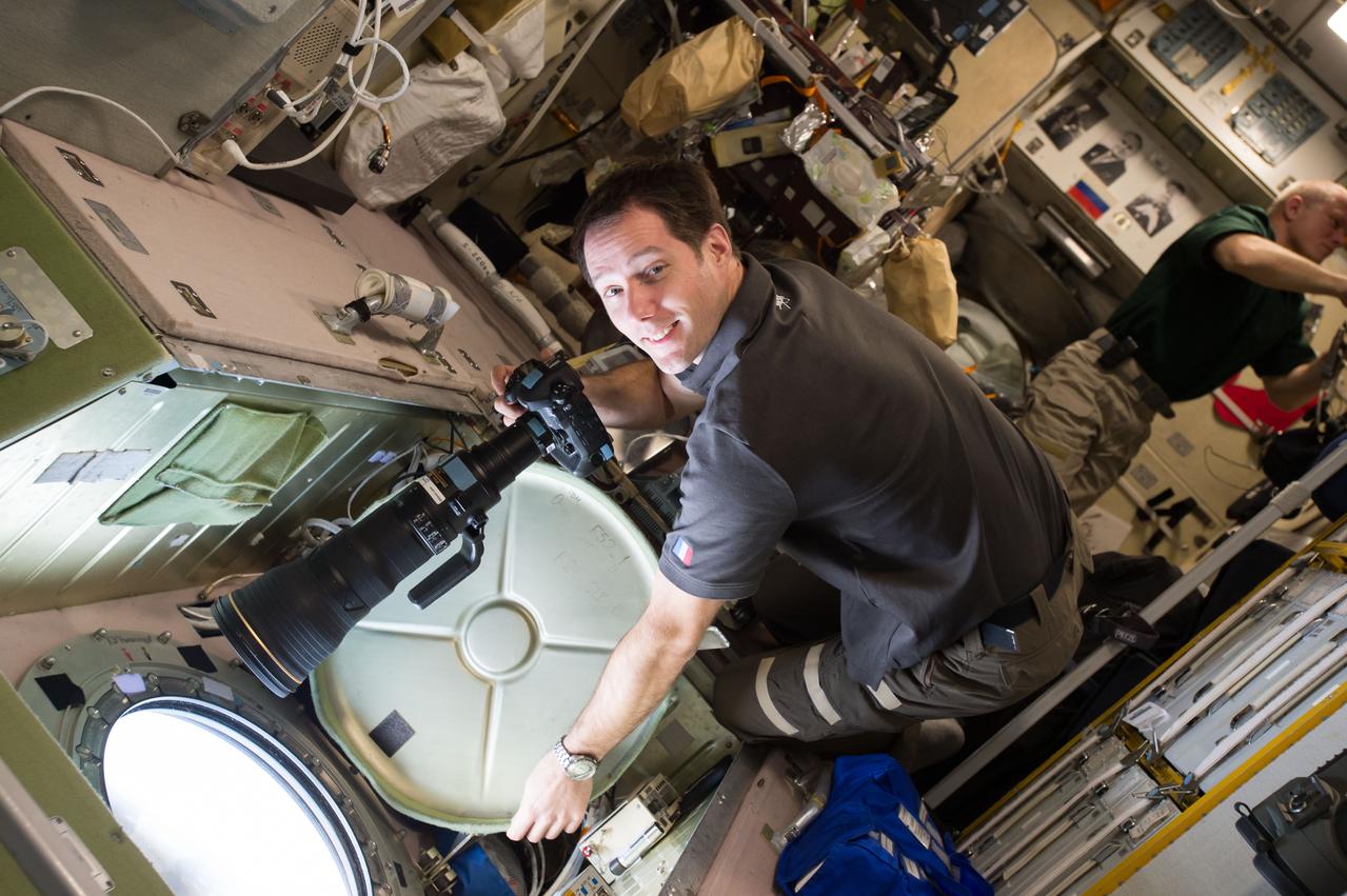 iss050e020100 (12/28/2016) --- European Space Agency (ESA) astonaut Thomas Pesquet preparing to take Crew Earth Observations (CEO) photos from the Service Module (SM) window. Cosmonaut Oleg Novitskiy is visible in the background. CEO imagery provides researchers on Earth with key data to understand the planet from the perspective of the ISS. Crew members have been photographing Earth from space since the early Mercury missions beginning in 1961. The images taken from the ISS ensure this record remains unbroken.