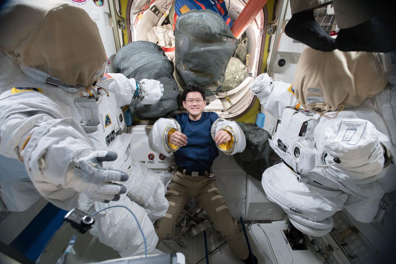 iss054e014016 (Jan. 2, 2018) --- Astronaut Norishige Kanai of the Japan Aerospace Exploration Agency tries on a pair of spacesuit sleeves inside the Quest airlock. To either side of Kanai are the U.S. spacesuits that were being readied for a pair of robotics maintenance spacewalks.