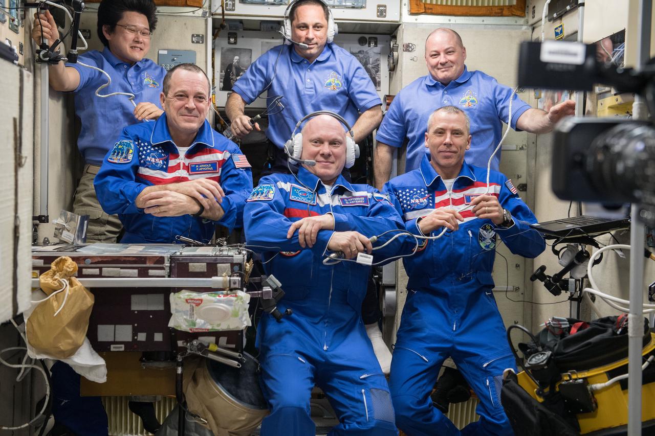 iss055e004863 (March 23, 2018) --- The newly-expanded Expedition 55 crew gathers inside the Zvezda service module with its three newest crew members in the front row for a welcoming ceremony shortly after they arrived March 23, 2018. In front from left are Flight Engineers Ricky Arnold, Oleg Artemyev and Drew Feustel. In the back from left are Flight Engineer Norishige Kanai, Commander Anton Shkaplerov and Flight Engineer Scott Tingle.