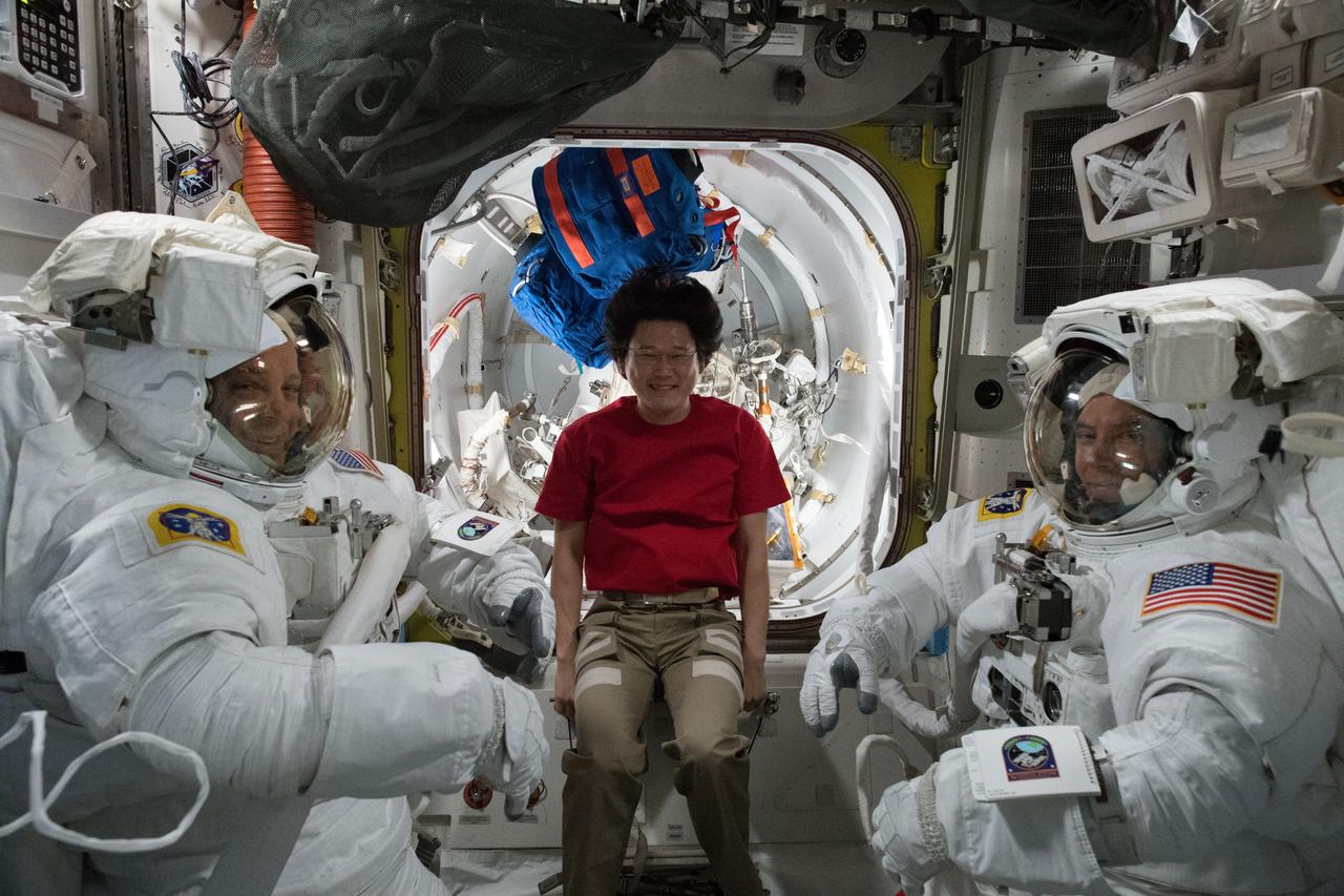 iss055e063888 (May 7, 2018) --- NASA astronauts Ricky Arnold (left) and Drew Feustel are pictured inside their U.S. spacesuits for a fit check verification ahead of a pair of spacewalks. Norishige Kanai (center), from the Japan Aerospace Exploration Agency, assisted the duo in and out of the spacesuits during the sizing process.
