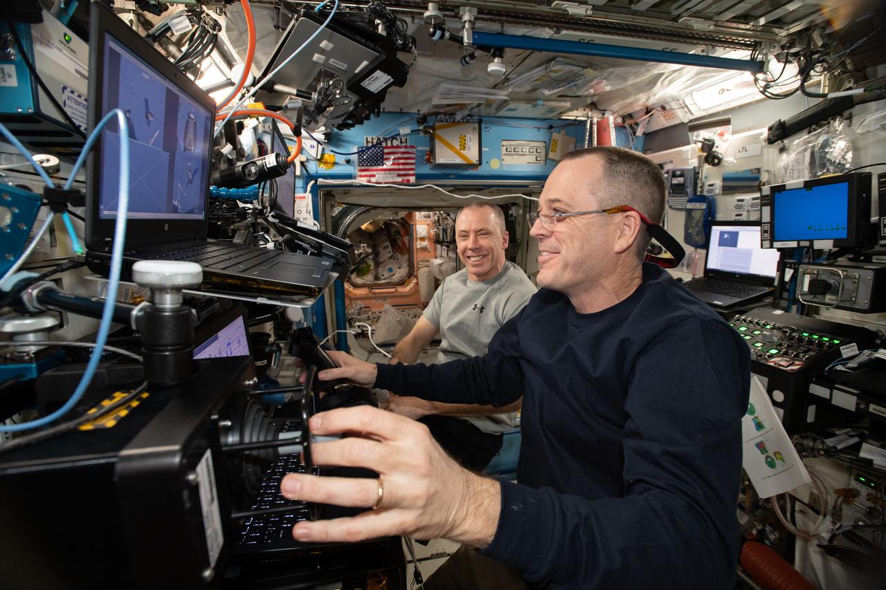 iss056e037500 (June 26, 2018) --- NASA astronauts Ricky Arnold (foreground) and Drew Feustel practice on a computer before their upcoming robotic maneuvers to capture the SpaceX Dragon cargo craft upon its arrival at the International Space Station on July 2, 2018.