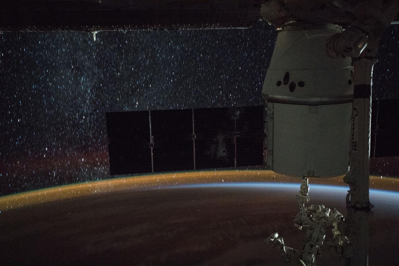 iss056e077457 (July 4, 2018) --- A star-lit sky and Earth's atmospheric glow are the backdrop as the Canadarm2 robotic arm, with its Dextre robotic hand attached, is poised to begin extracting cargo from the rear of the SpaceX Dragon cargo craft, or it's trunk.