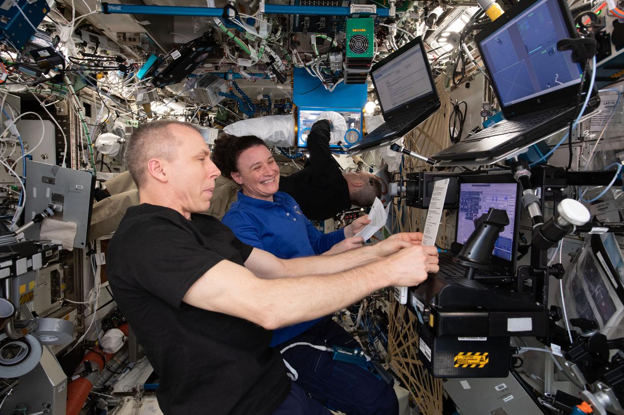 iss056e161212 (Sept. 6, 2018) --- Astronauts Drew Feustel and Serena Auñón-Chancellor train on a computer in the U.S. Destiny laboratory practicing rendezvous procedures and robotics maneuvers ahead of the arrival of Japan's HTV-7 resupply ship. In the background, astronaut Ricky Arnold works on the Rodent Research Habitat feeding mice and cleaning cameras.