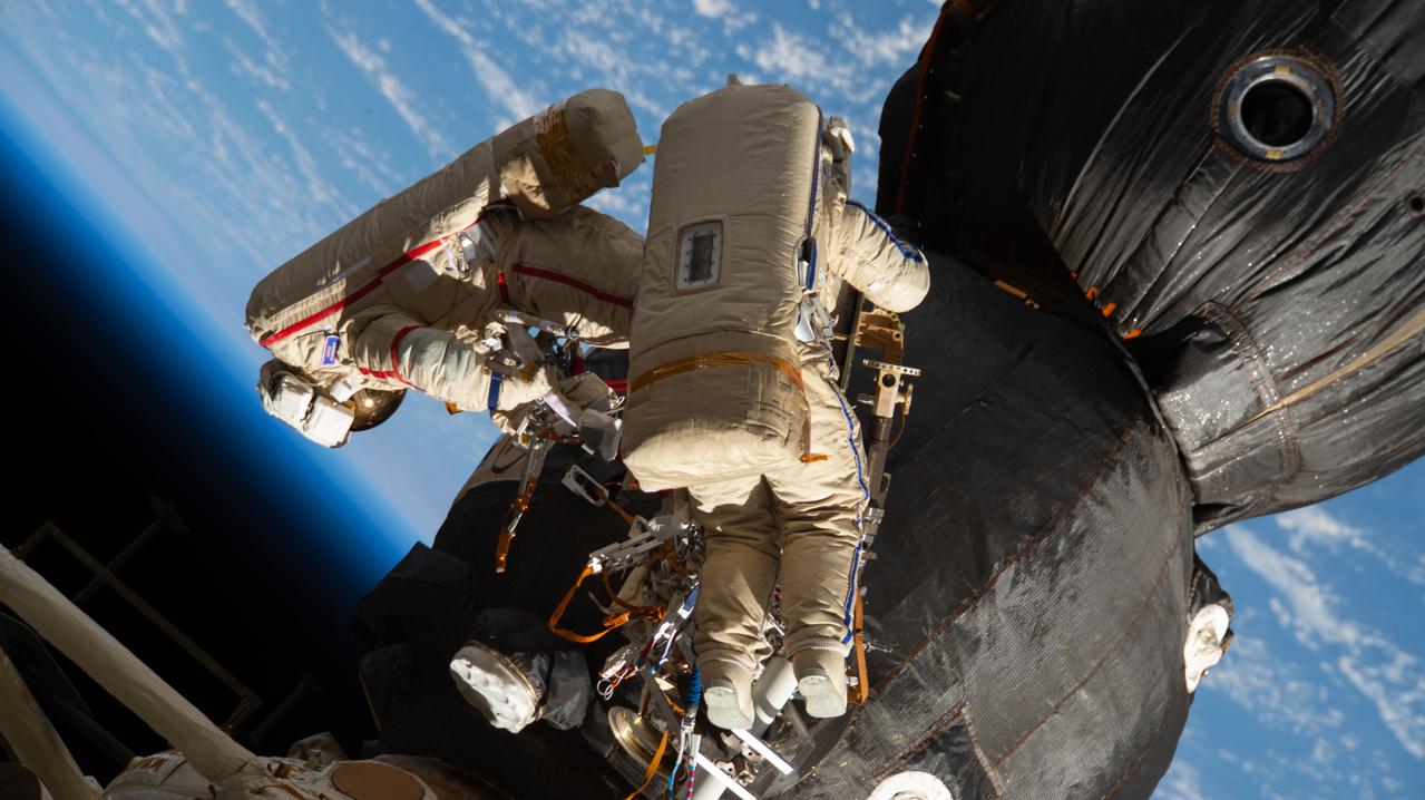 iss057e131663 (Dec. 11, 2018) --- Russian spacewalkers Oleg Kononenko (suit with red stripes) and Sergey Prokopyev (suit with blue stripes) work outside the International Space Station over 250 miles above Earth to inspect the Soyuz MS-09 spacecraft. During the spacewalk, the two examined the external hull of the Soyuz crew ship docked to the Rassvet module, took images and applied a thermal blanket. They also retrieved science experiments before heading back inside the Pirs docking compartment and closing the hatch completing a seven-hour, 45-minute spacewalk.the duo examined the external hull of the Soyuz crew ship docked to the Rassvet module. The area corresponded with the location of a small hole inside the Soyuz habitation module that was found in August and caused a decrease in the space station’s pressure. The hole was fixed internally with a sealant within hours of its detection. During the spacewalk, Kononenko and Prokopyev collected samples of some of the sealant that extruded through hole to the outer hull before heading back inside the Pirs docking compartment and closing the hatch completing a seven-hour, 45-minute spacewalk.