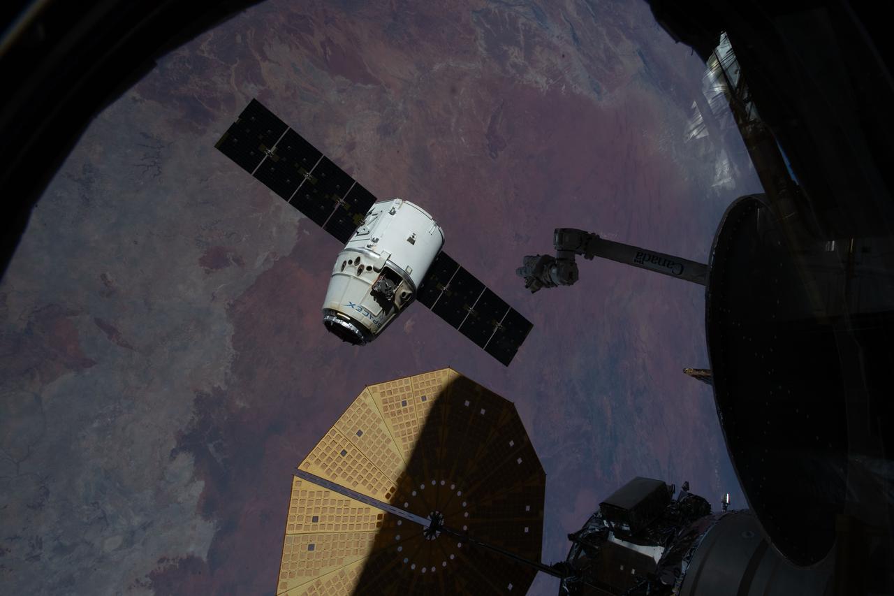 iss058e002813 (Jan. 13, 2019) --- The SpaceX Dragon cargo craft begins its departure from the International Space Station moments after being released from the grips of the Canadarm2 robotic arm. Featured prominently in the lower foreground is one of two cymbal-shaped UltraFlex solar arrays attached to the Northrop Grumman Cygnus resupply ship. The orbital complex was orbiting 255 miles above Australia's Northern Territory at the time this photograph was taken.