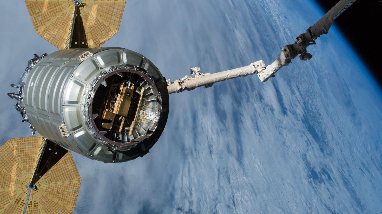 iss058e011401 (Feb. 8, 2019) --- The Cygnus cargo craft from Northrop Grumman with its prominent cymbal-shaped UltraFlex solar arrays is pictured in the grips of the Canadarm2 robotic arm. Cygnus would be released moments later as the International Space Station was orbiting over the Pacific Ocean. Visible in Cygnus' Common Berthing Mechanism is the Slingshot small satellite deployer designed to deploy CubeSats from the cargo ship once it reaches a safe distance from the station after its release.