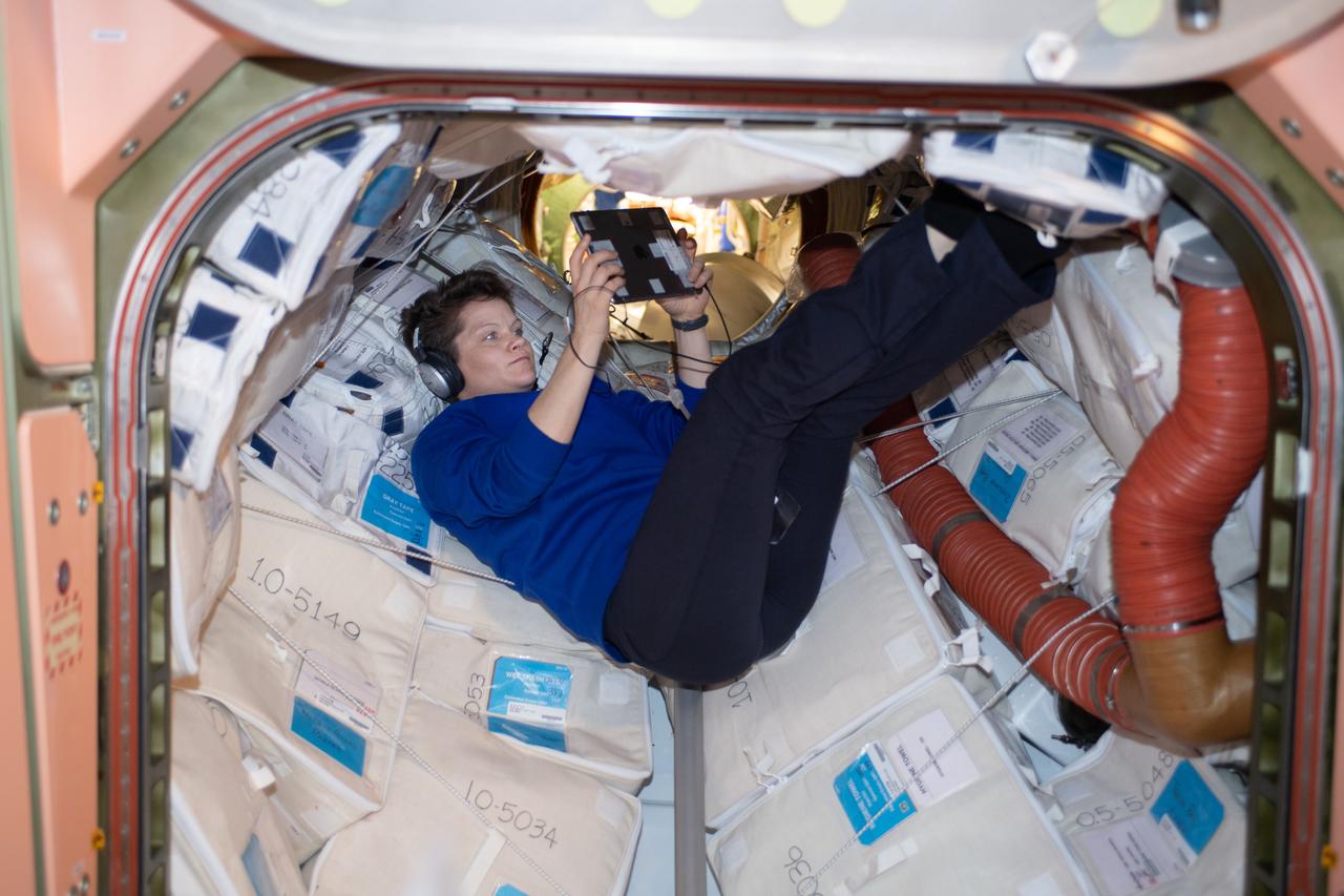iss059e027379 (April 21, 2019) --- NASA astronaut Anne McClain relaxes with an electronic tablet on a Sunday morning inside the vestibule that connects the Unity module to the Zarya module.