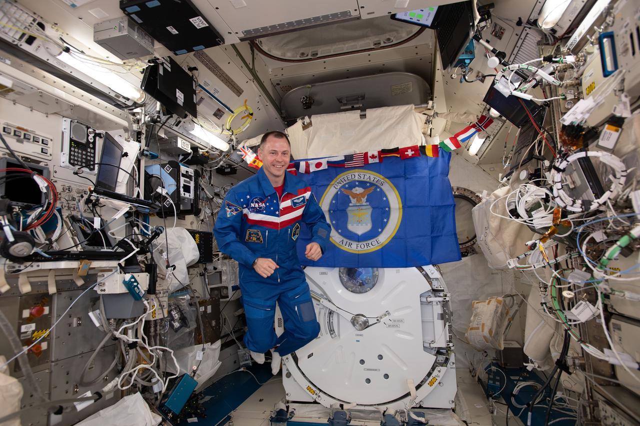 iss059e042272 (April 30, 2019) --- NASA astronaut Nick Hague poses for a portrait with the insignia of the United States Air Force behind him aboard the International Space Station.