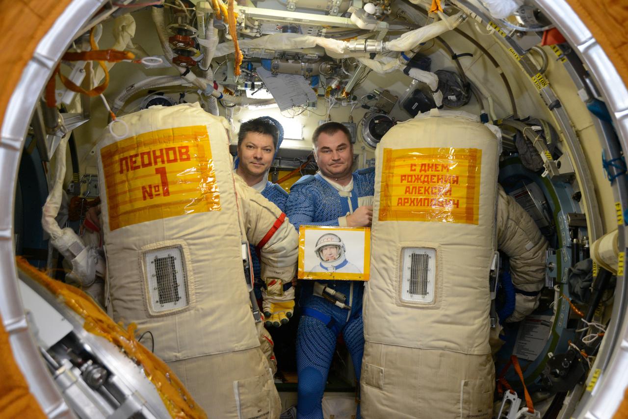 iss059e072908 (May 26, 2019) --- Cosmonauts Oleg Kononenko (left) and Alexey Ovchinin commemorated Alexei Leonov, the first human to walk in space, who turns 85 on Thursday, with signs attached to their Orlan spacesuits during their May 29, 2019, spacewalk. The sign attached to the spacesuit at left translates to, "Leonov #1." The sign on the spacesuit at right says, “Happy Birthday, Alexei Arkhipovich,” (Leonov’s patronymic name).