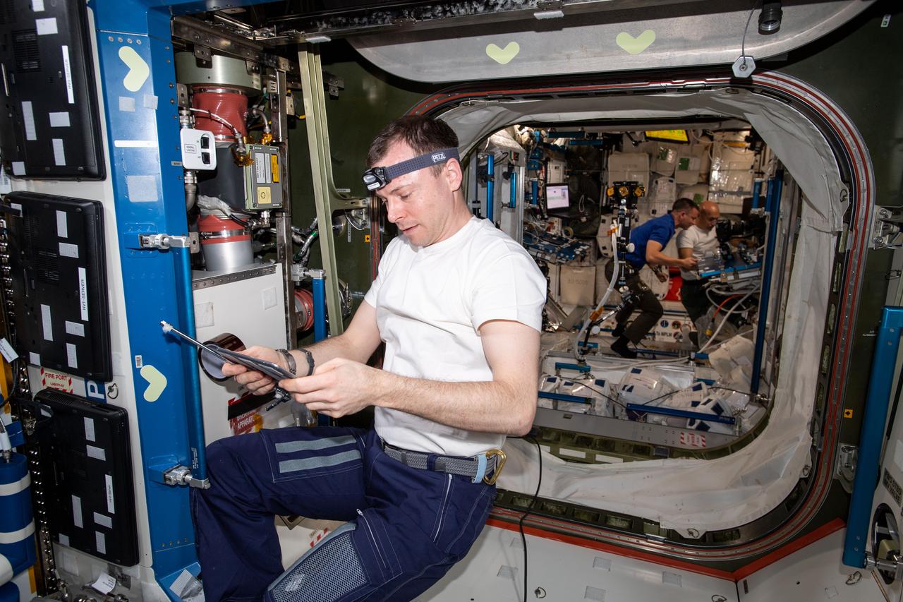 iss060e014222 (July 24, 2019) --- Expedition 60 Flight Engineer Nick Hague of NASA concentrates on life support maintenance work inside the U.S. Destiny laboratory module. Behind Hague in the Harmony module, are Flight Engineers Andrew Morgan and Luca Parmitano familiarizing themselves with International Space Station systems having been in space less than week.