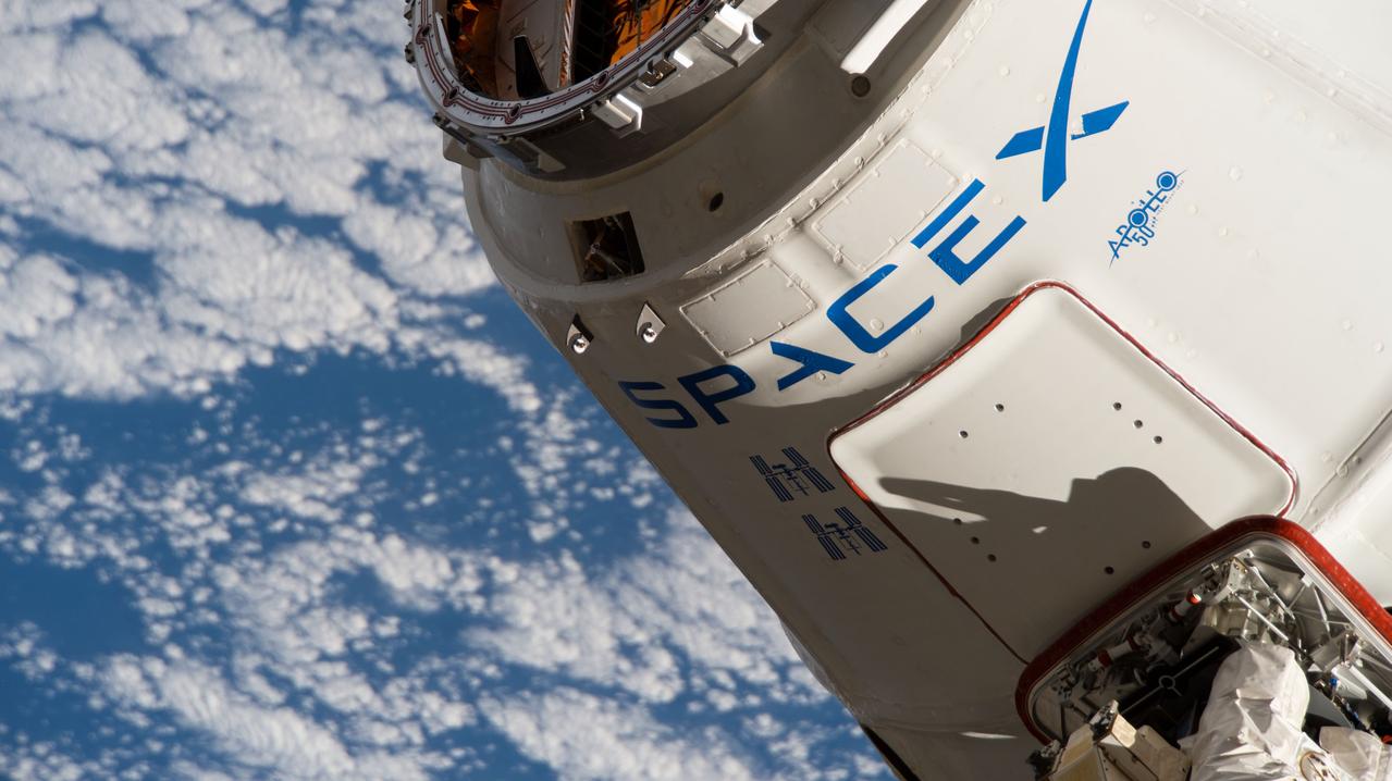 iss060e014962 (July 27, 2019) --- The re-usable SpaceX Dragon space freighter is in the grips of the Canadarm2 robotic arm shortly after it was captured following a day-and-a-half-long trip that began with a launch from Cape Canaveral, Florida. This was the third flight of this individual spacecraft with its previous flights denoted by two insignia depicting the International Space Station. The Apollo 50th anniversary insignia is also highlighted on the commercial resupply ship.