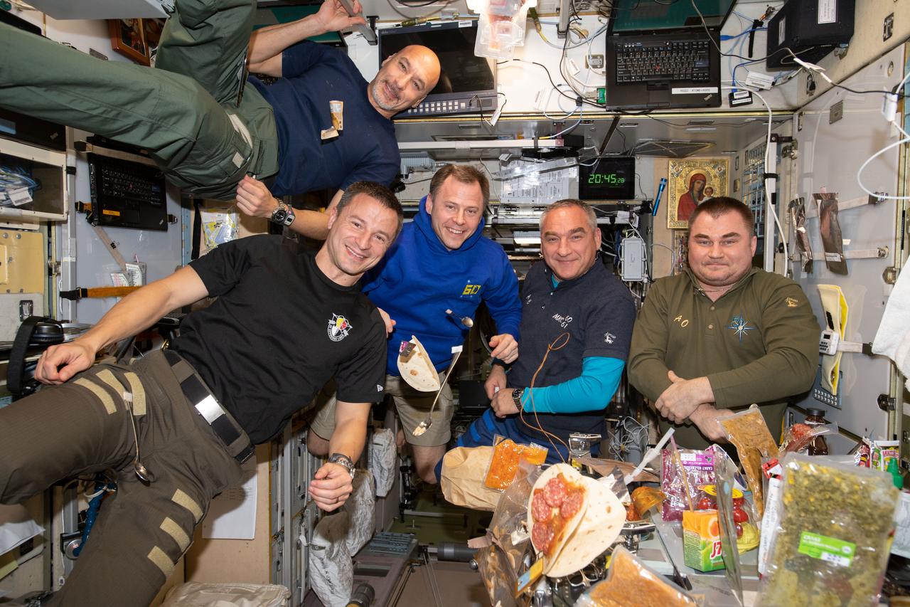 iss060e021619 (Aug. 2, 2019) --- It's dinner time aboard the International Space Station as five Expedition 60 crewmembers gather inside the Zvezda service module's galley. At top is Luca Parmitano of the European Space Agency. In front, from left, are NASA astronauts Andrew Morgan and Nick Hague and Roscosmos cosmonauts Alexander Skvortsov and Alexander Skvortsov.