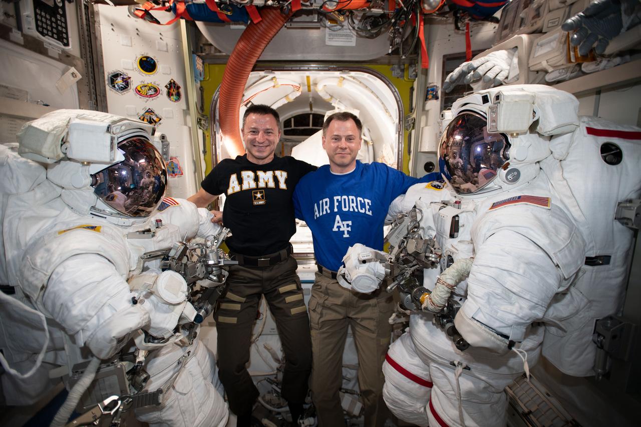 iss060e037335 (Aug. 18, 2019) --- NASA astronauts Andrew Morgan and Nick Hague pose with the spacesuits they will wear during a six-and-a-half-hour spacewalk to install the International Docking Adapter-3 that will accommodate the future arrivals of Boeing CST-100 Starliner and SpaceX Crew Dragon commercial crew spacecraft.