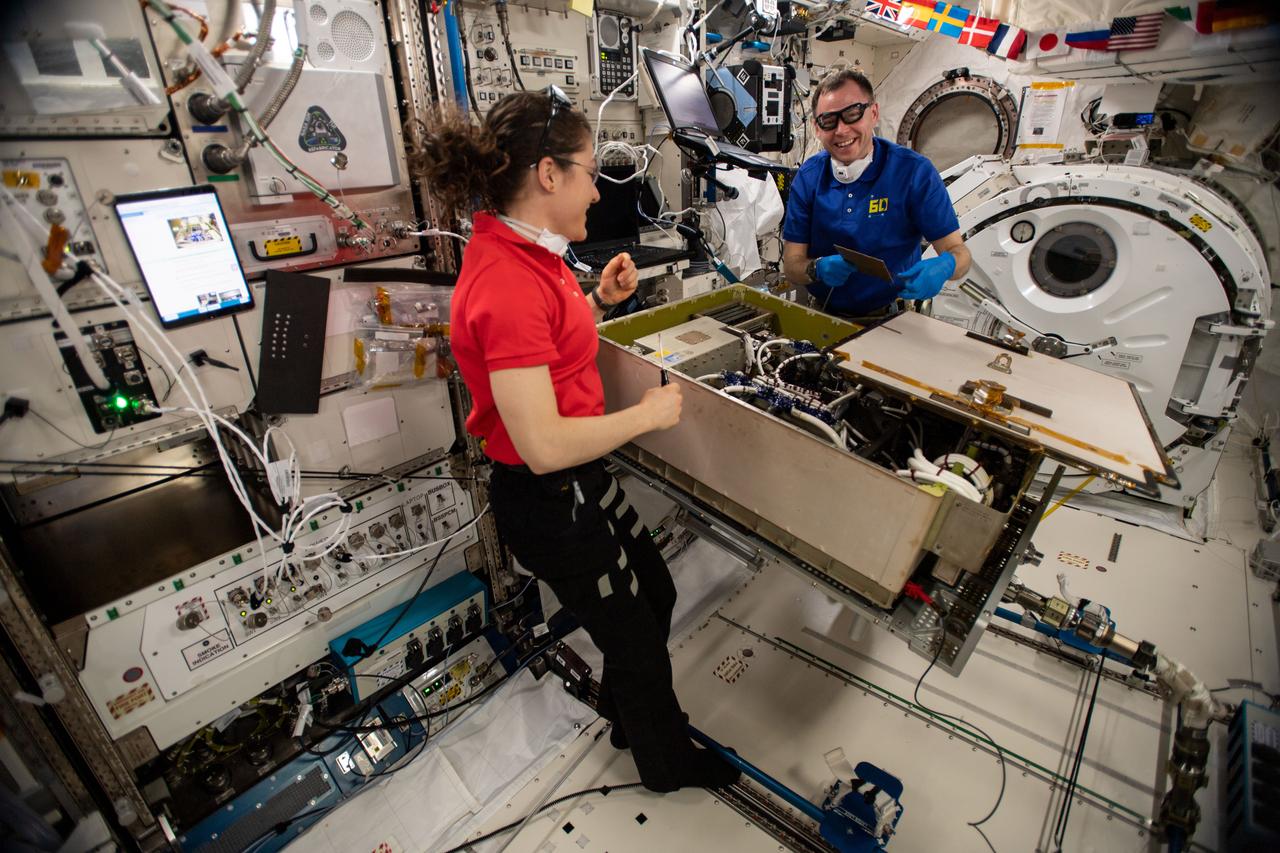 Expedition 60 flight engineers Christina Koch and Nick Hague of NASA work together on the Main Bus Switching Unit aboard the space station to replace a failed circuit card before performing a test to ensure its functionality.