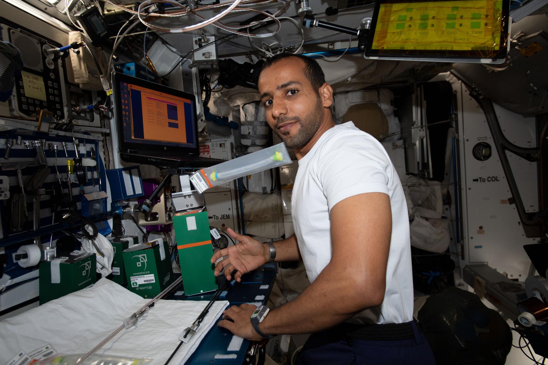An astronaut in a white shirt conducts experiments at a console on the the international space station