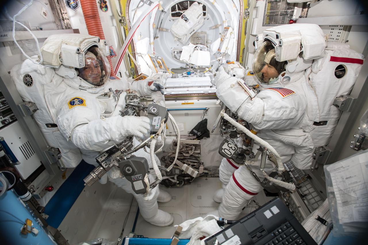 iss061e001577 (Oct. 6, 2019) --- NASA astronauts Andrew Morgan (left) and Christina Koch (right) are suited up in U.S. spacesuits inside the Quest airlock before beginning a seven hour and one minute spacewalk to upgrade the station's large nickel-hydrogen batteries with newer, more powerful lithium-ion batteries.