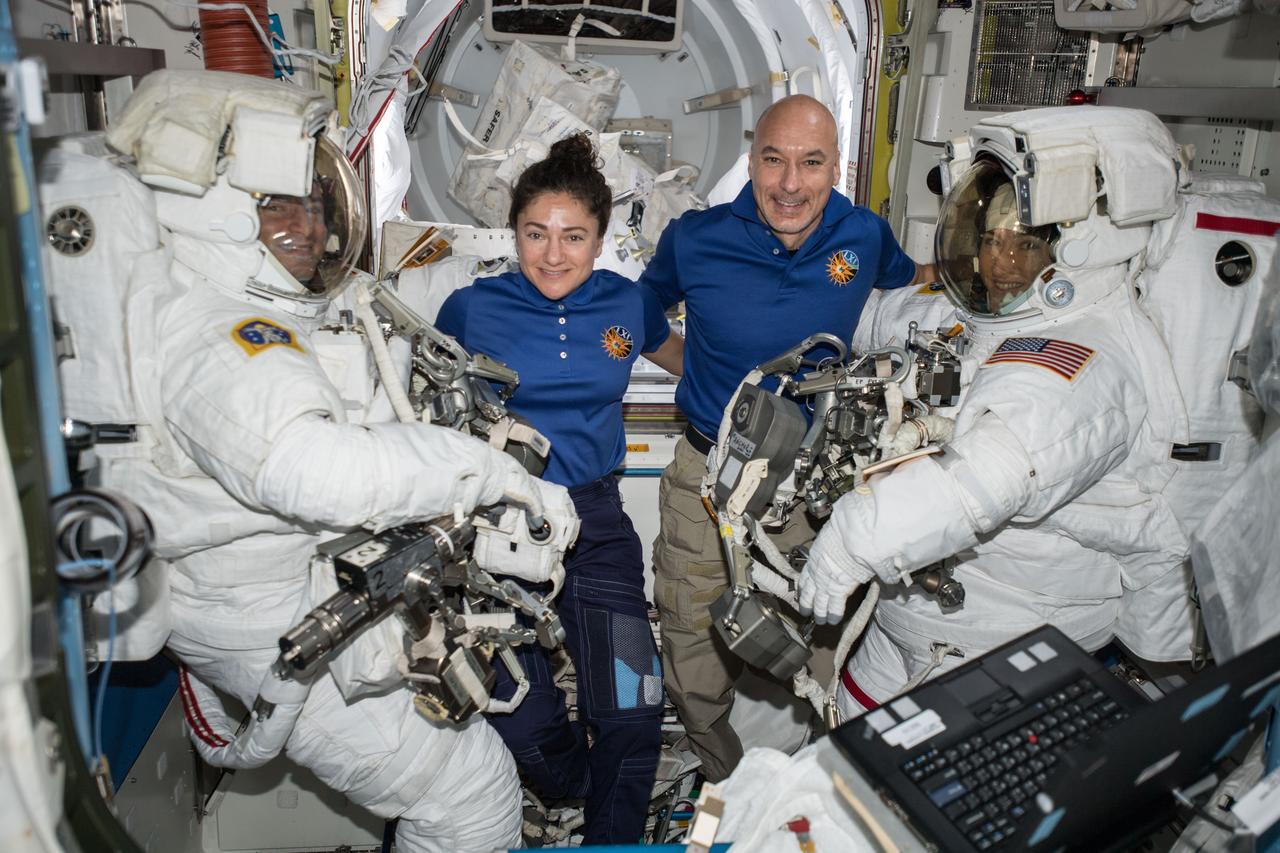 iss061e001608 (Oct. 6, 2019) --- NASA astronauts Andrew Morgan (left) and Christina Koch (right) are suited up in U.S. spacesuits before beginning a seven hour and one minute spacewalk to upgrade the station's large nickel-hydrogen batteries with newer, more powerful lithium-ion batteries. In the center, NASA Flight Engineer Jessica Meir and Commander Luca Parmitano of ESA (European Space Agency) assist the spacewalking duo.