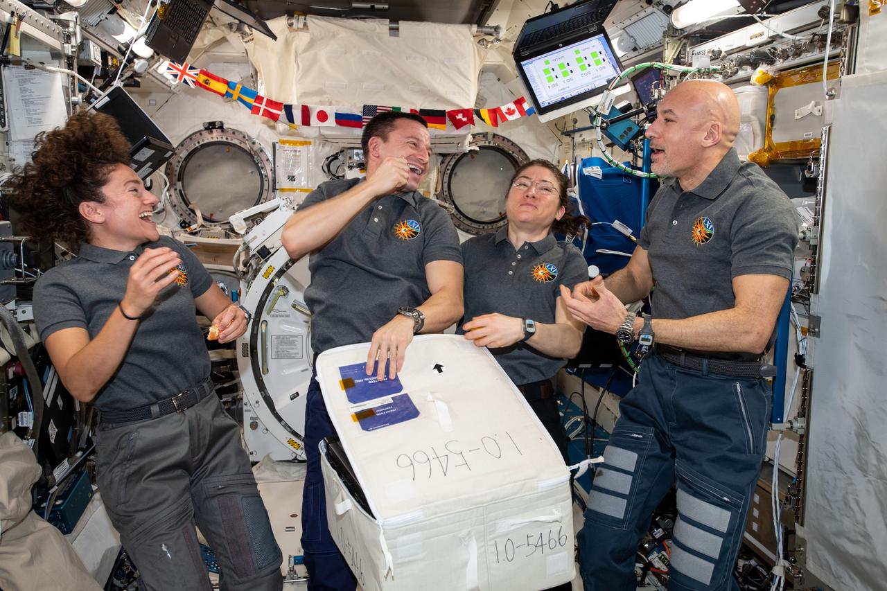 iss061e003995 (Oct. 7, 2019) --- Four Expedition 61 crewmembers open a stowage case packed with fresh fruit and other goodies delivered aboard Japan's HTV-8 cargo craft. From left are, NASA Flight Engineers Jessica Meir, Andrew Morgan and Christina Koch with Commander Luca Parmitano of ESA (European Space Agency).